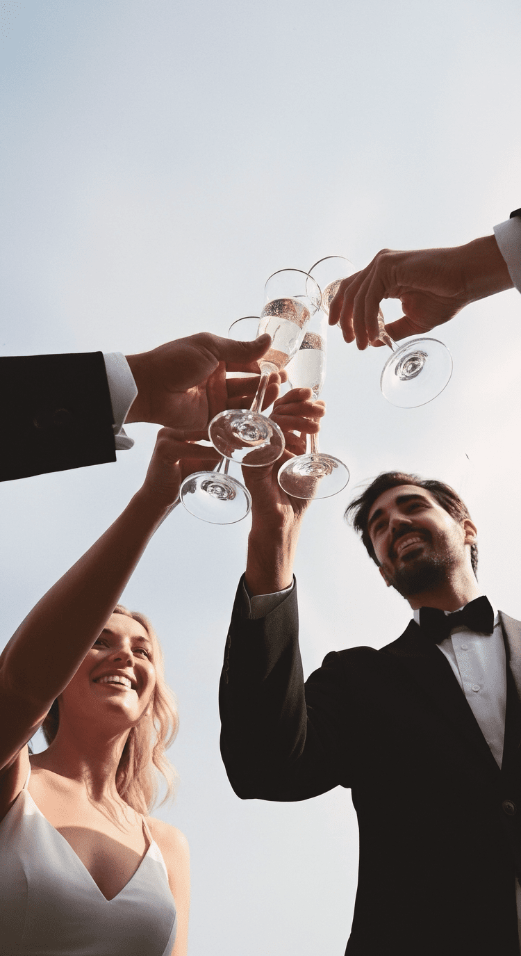 People in formal attire celebrating and toasting with champagne glasses outdoors.