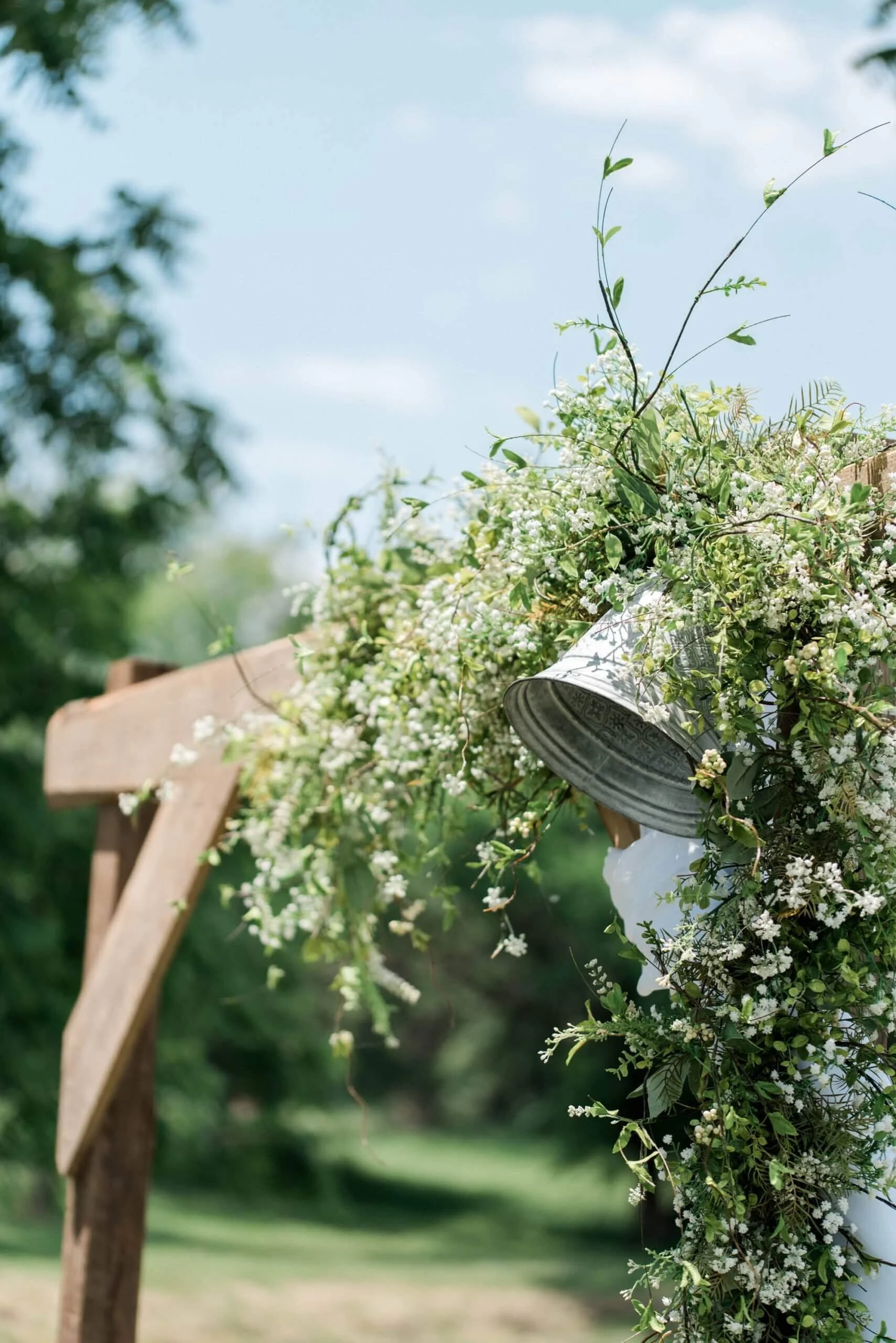 Close-up of an outdoor decoration with white flowers and green leaves attached to a wooden structure, against a background of a grassy yard and blue sky.