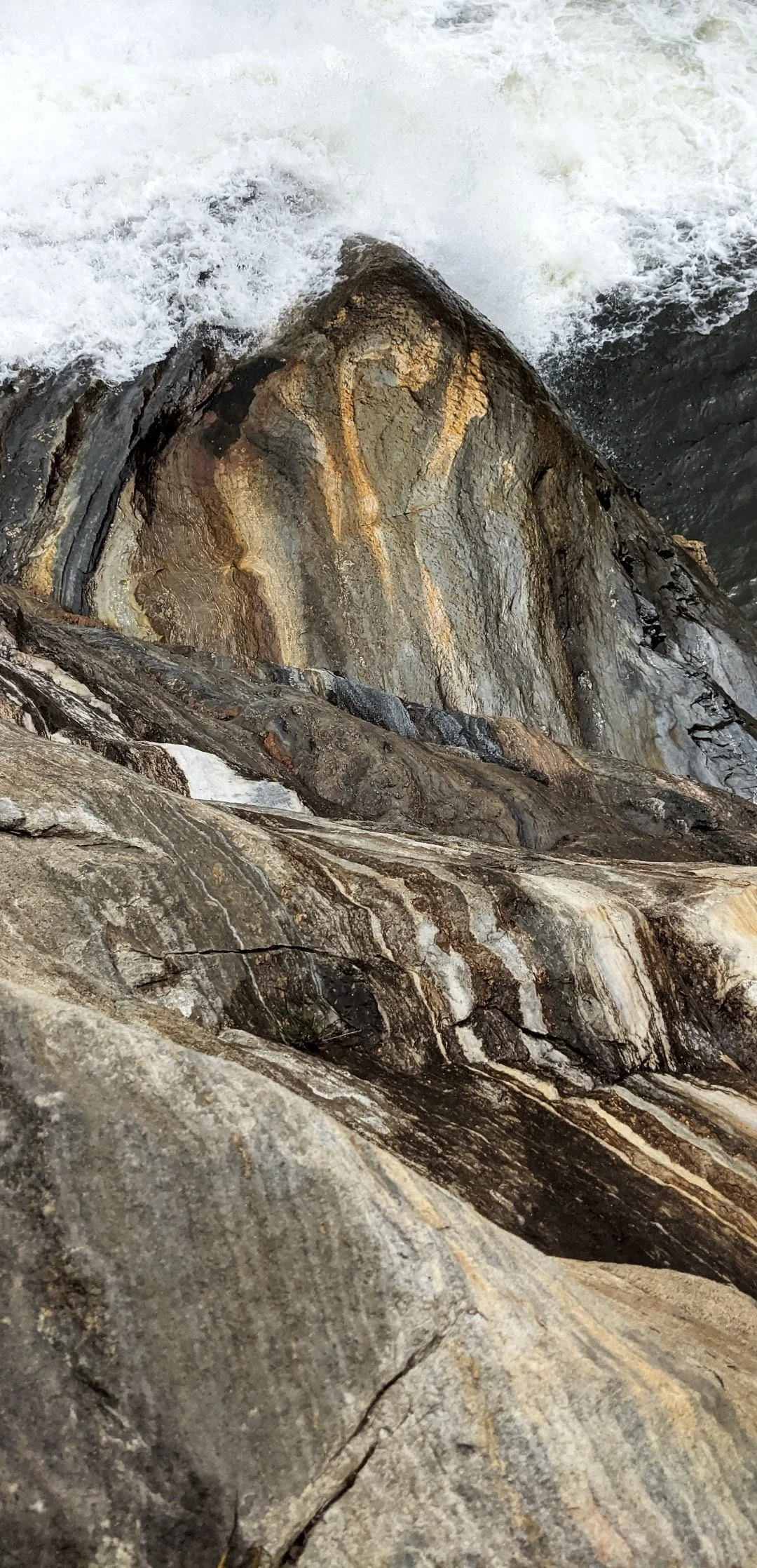 A large rock formation with streaks of different colors, surrounded by water rushing over it.