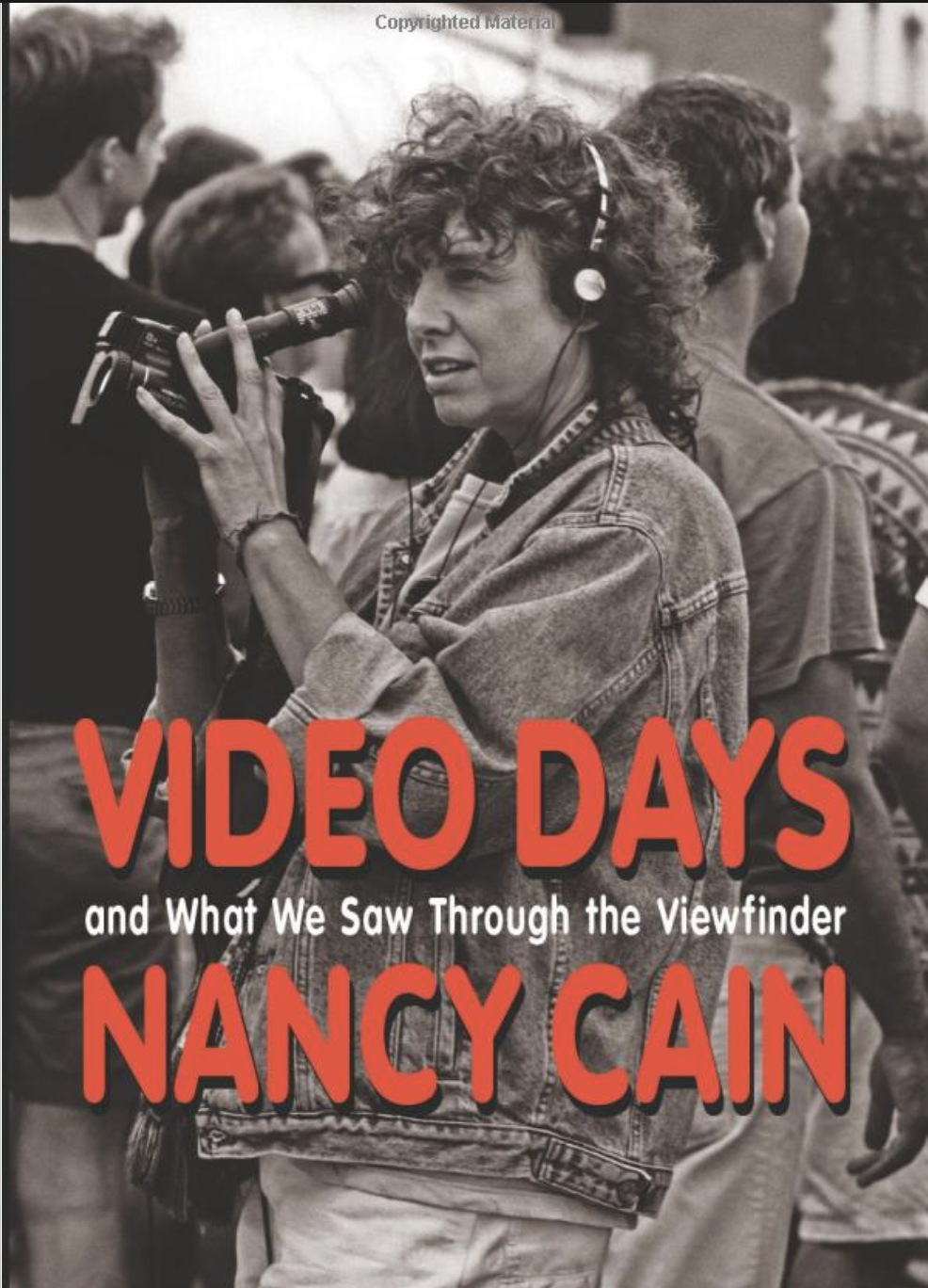A woman with curly hair wearing a denim jacket and headphones holding a video camera, surrounded by people in a crowd, in black and white with red and white text overlay.