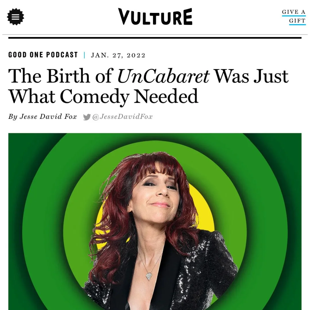 A woman with red hair, wearing a black sequined jacket and a heart-shaped pendant necklace, smiling confidently with a bold comic-style green and yellow concentric circle background.