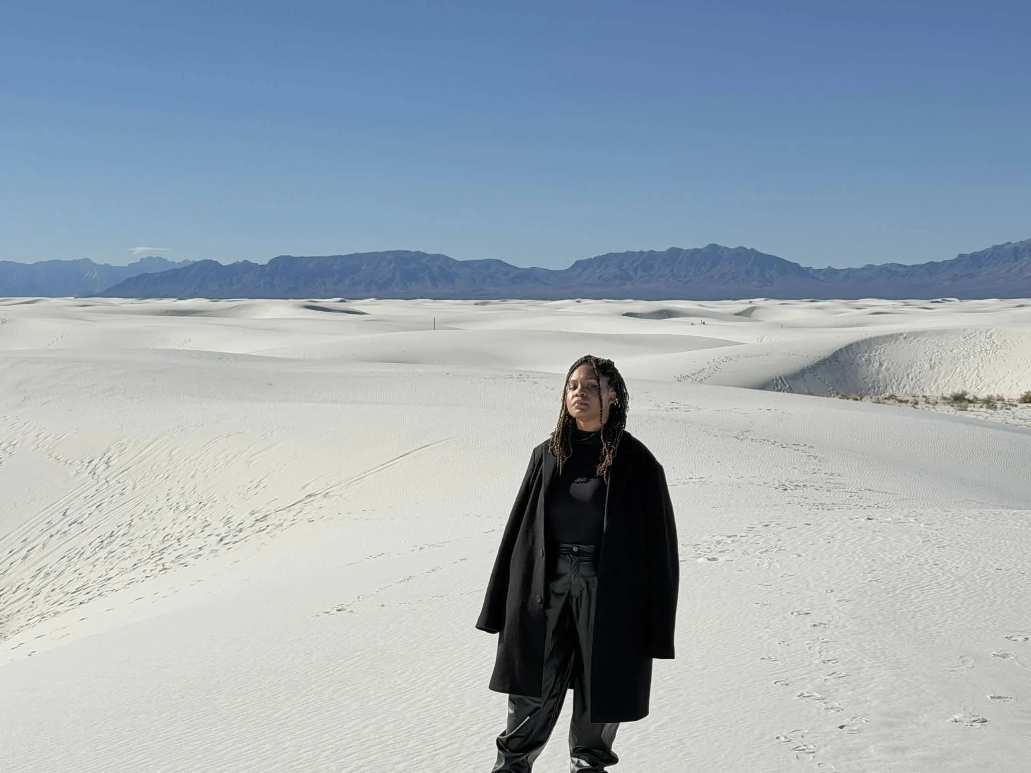 A person standing in a vast, white desert with mountains in the background under a clear blue sky.