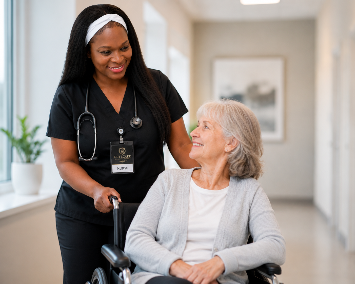 A nurse with a stethoscope around her neck and a name badge interacting with an elderly woman in a wheelchair; both are smiling at each other.