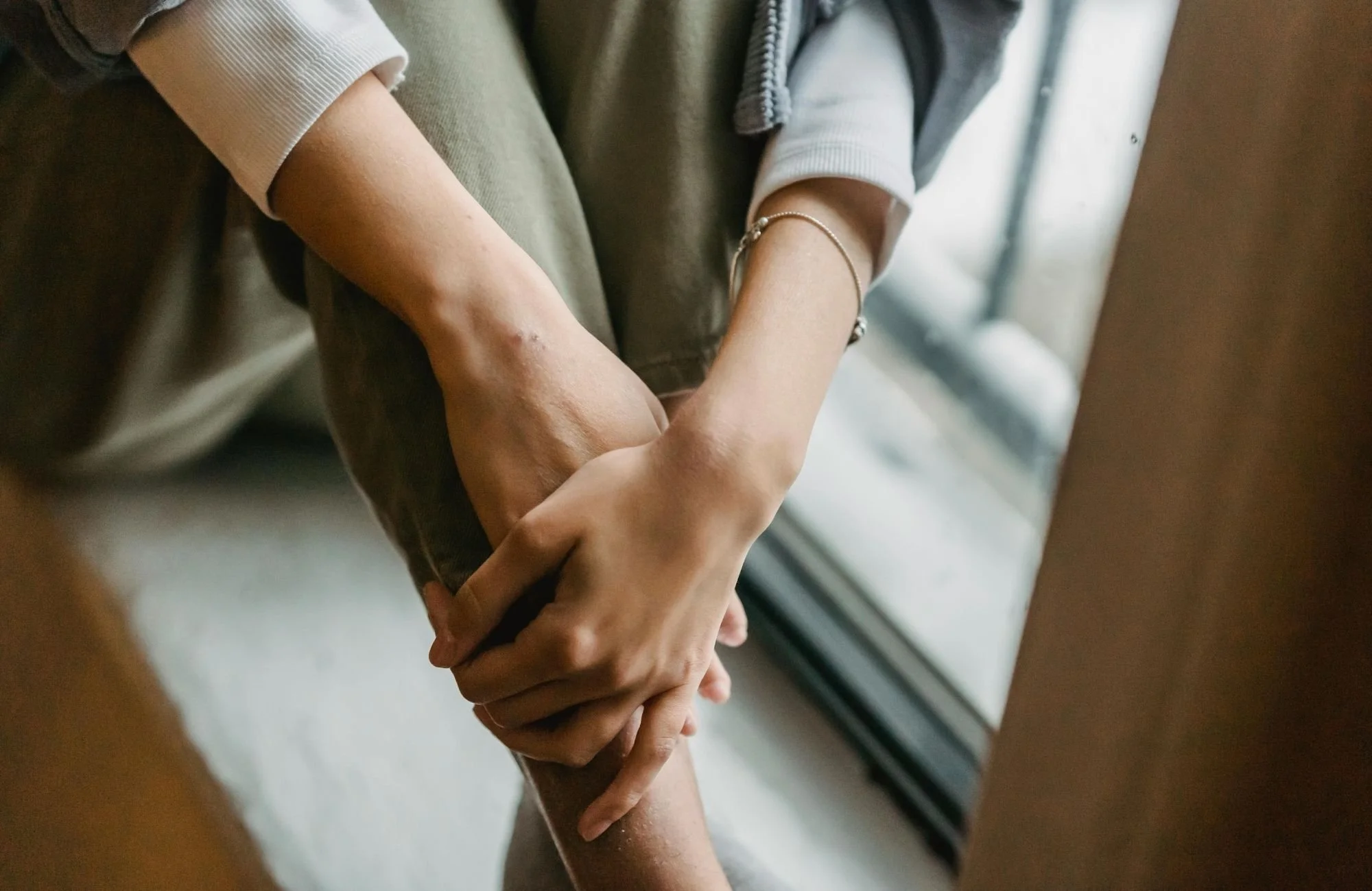 Two people holding hands near a window, focusing on their hands and arms.