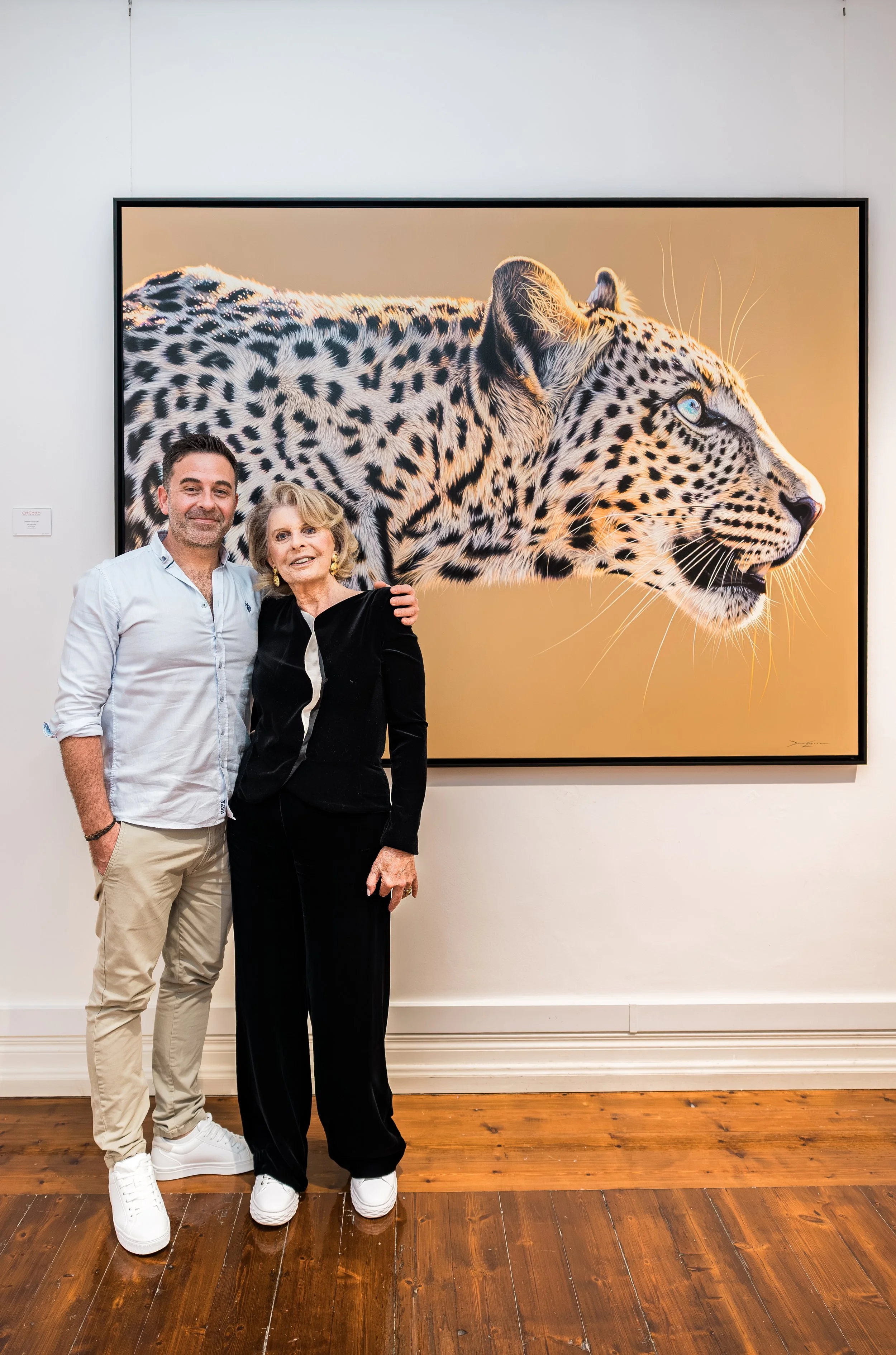 Darryn Eggleton, South African wildlife artist, with Gillian Catto, ArtCatto, Portugal. April 2026 Darryn Eggleton exhibition at ArtCatto. Both standing in front of an original oil painting of a Leopard, Only the Brave.