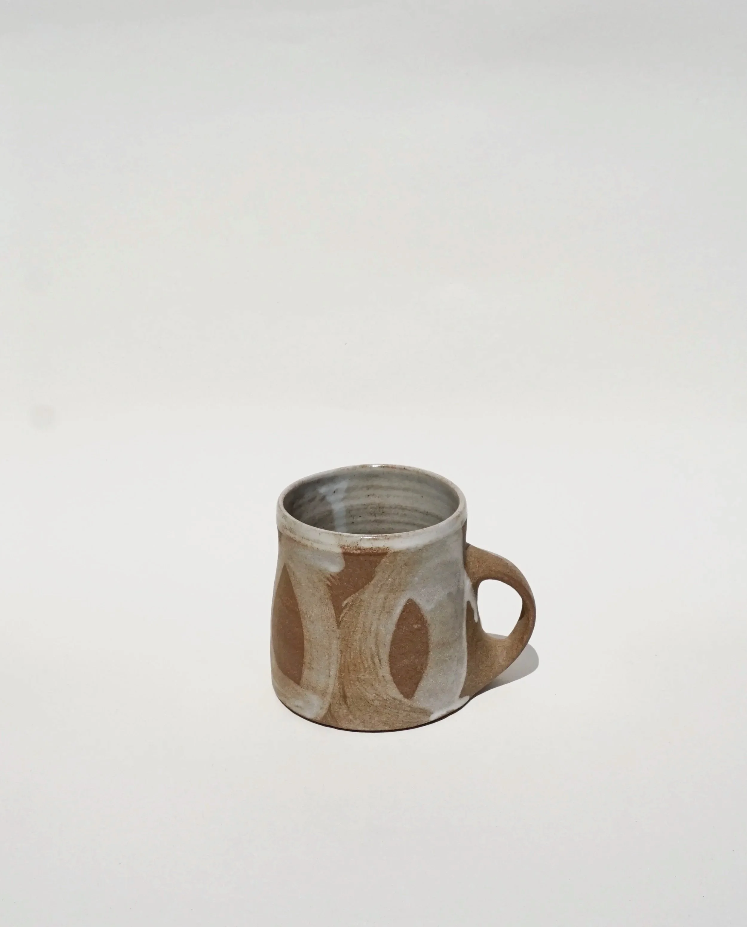 Stoneware tea mug with porcelain slip sweeping brushwork decoration and an exposed clay surface.