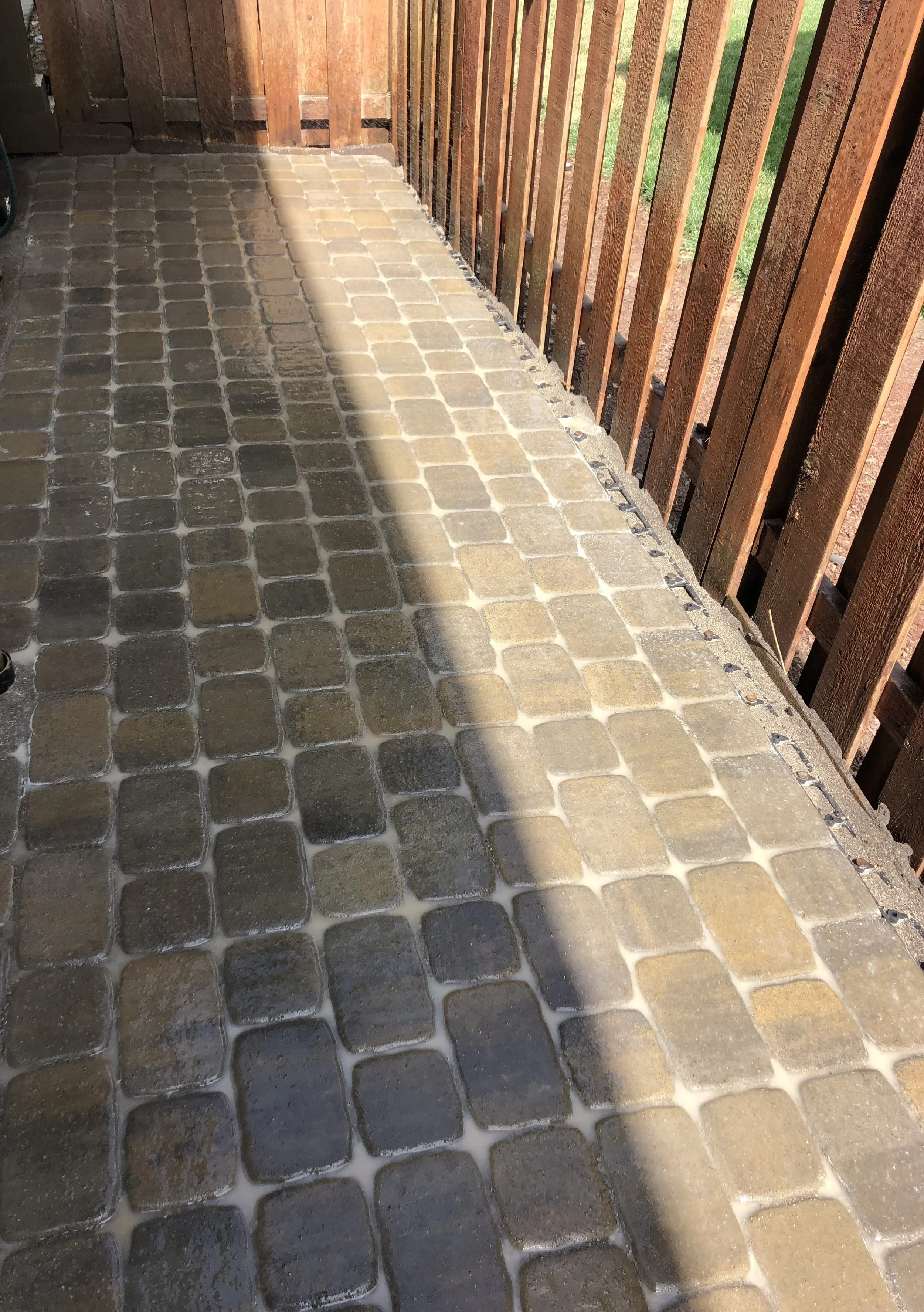 Cobblestone patio with a wooden fence on the right side, sunlight casting a shadow across the stones.