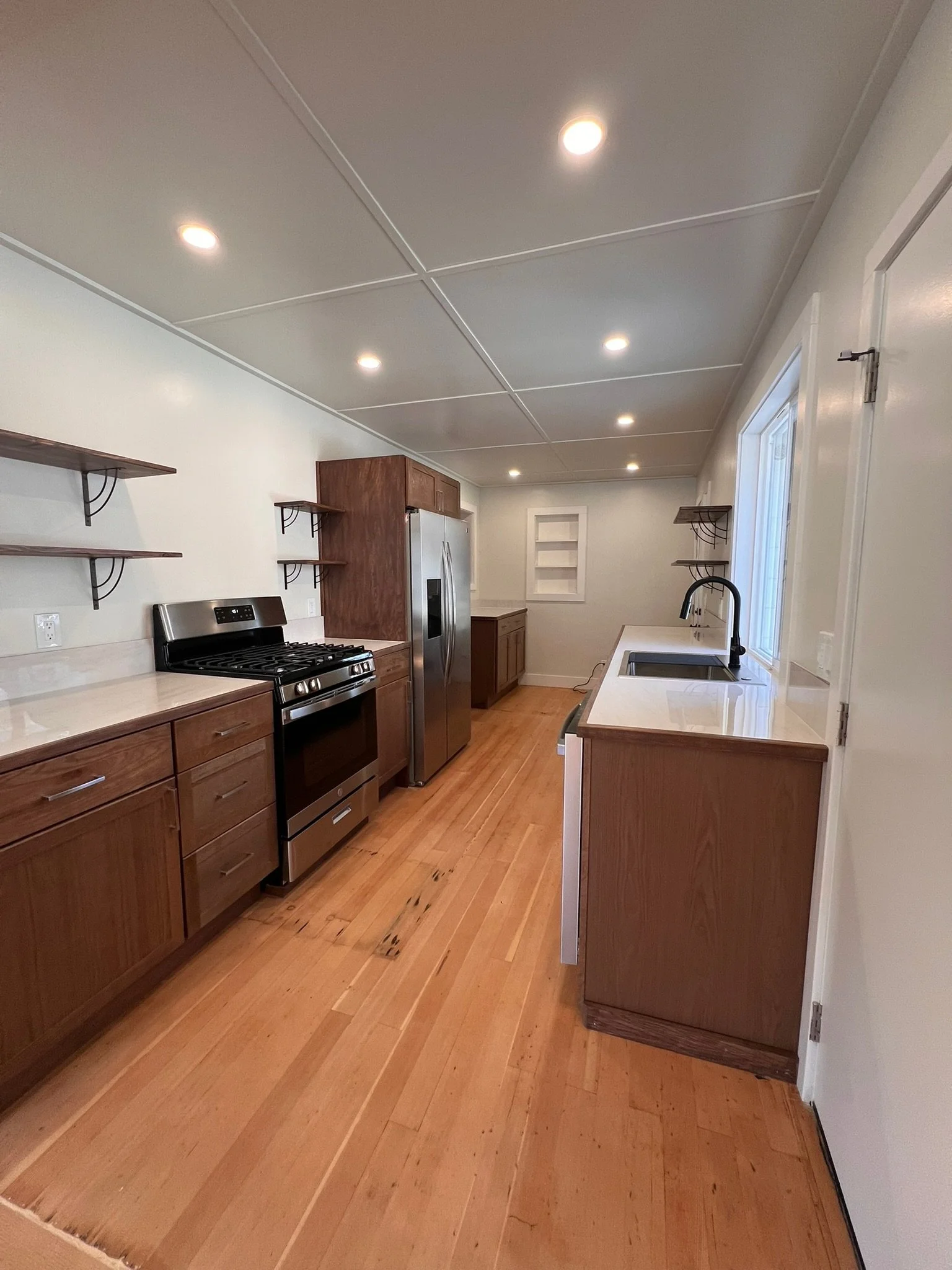 View of a modern kitchen with wooden cabinets, stainless steel appliances, a white countertop, and a ceiling with recessed lighting.