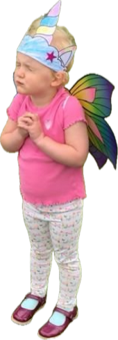 A young girl dressed as a fairy unicorn with a unicorn horn headband, rainbow-colored wings, and a pink shirt. She is standing with her eyes closed and hands together.