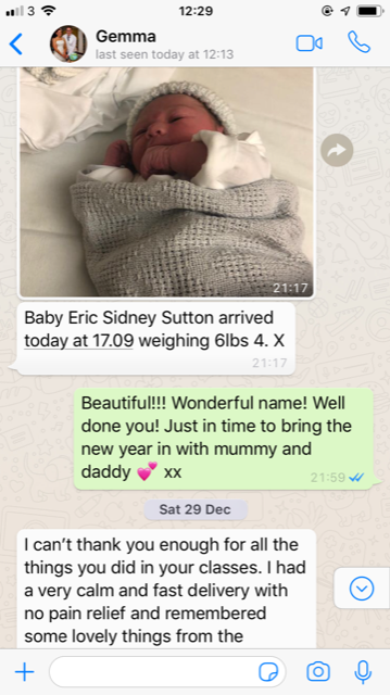Newborn baby wrapped in a gray blanket and wearing a knit hat, lying in bed.