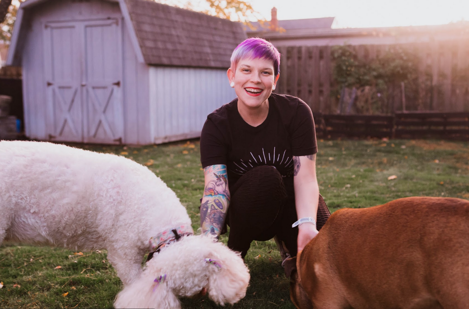 Woman with colorful hair rewards two dogs during pet training, smiling at the camera.