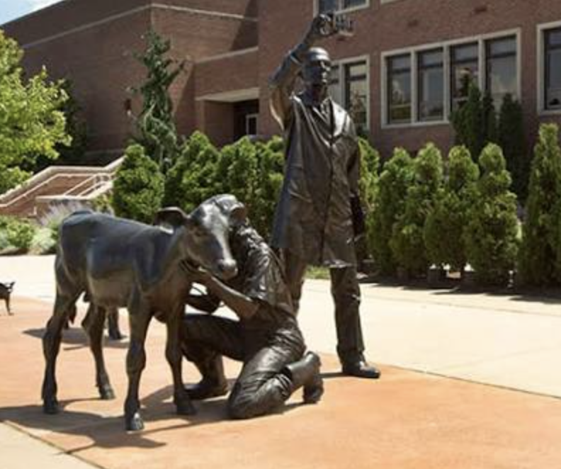 Bronze statues of a man and a woman with a cow and a calf in an outdoor setting.