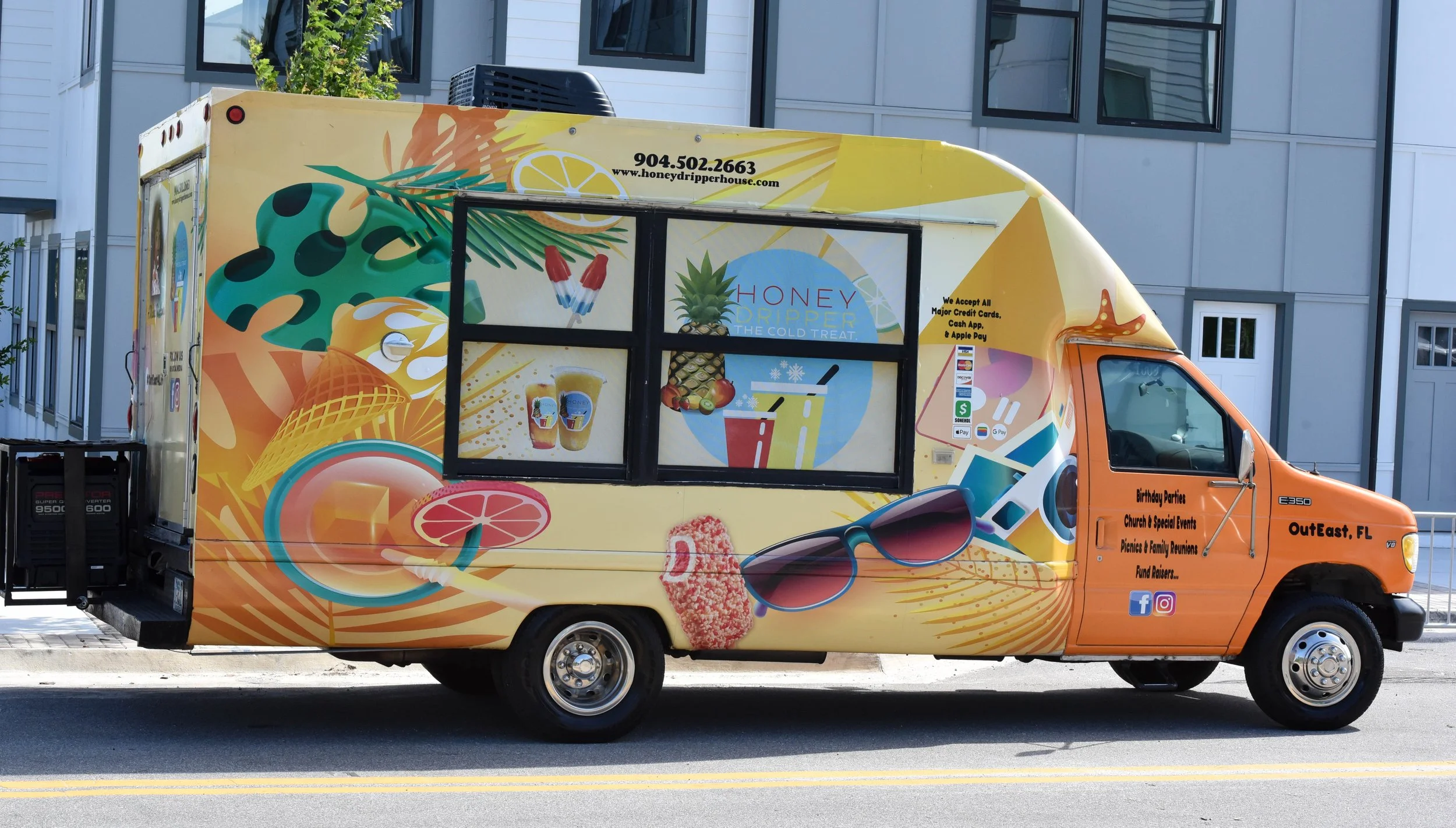 Colorful food truck with tropical and summer-themed decorations, advertising honey dripper drinks, ice cream, and popsicles, parked on a city street with residential buildings in the background.