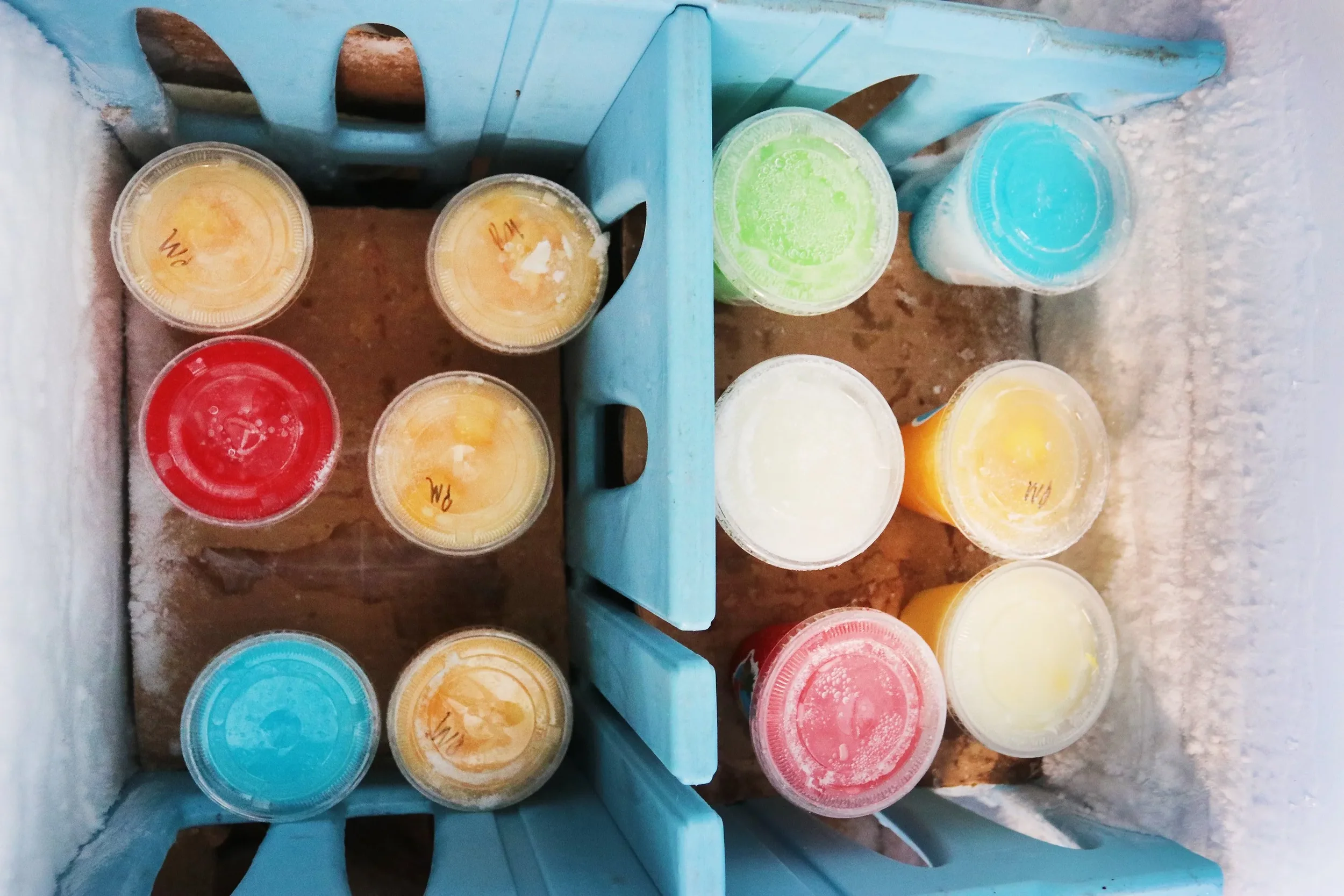 Assorted colorful smoothies in plastic cups arranged on a blue wooden tray.