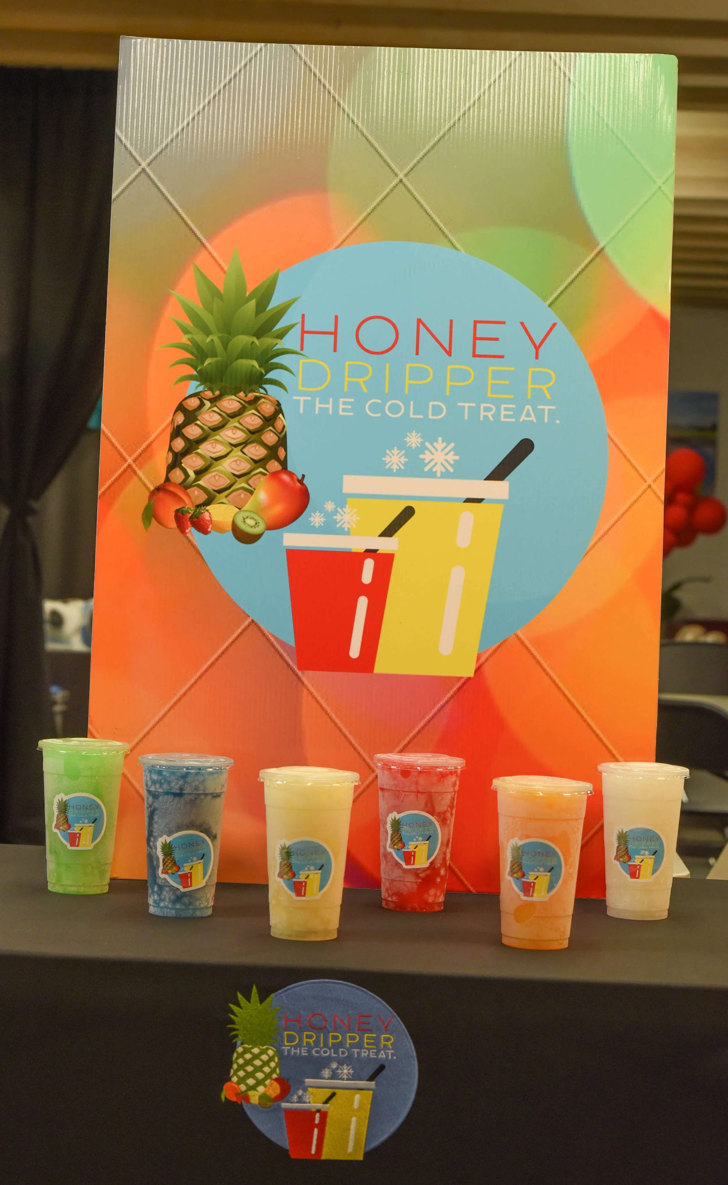 Display of colorful frozen drinks in cups with a pineapple and fruit decoration and a large sign advertising honey dripper, a cold treat with ice, for hot weather.