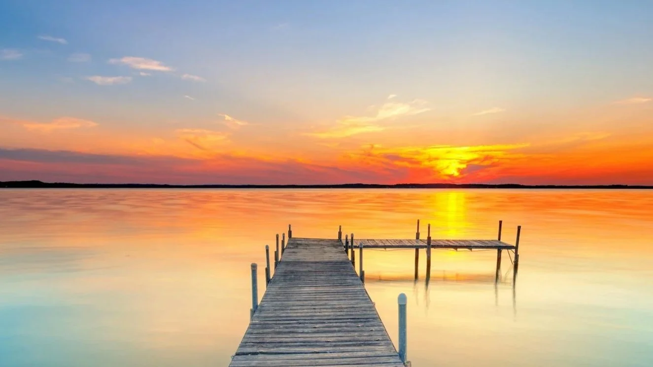 Sunset over a calm body of water with a wooden dock extending into the water