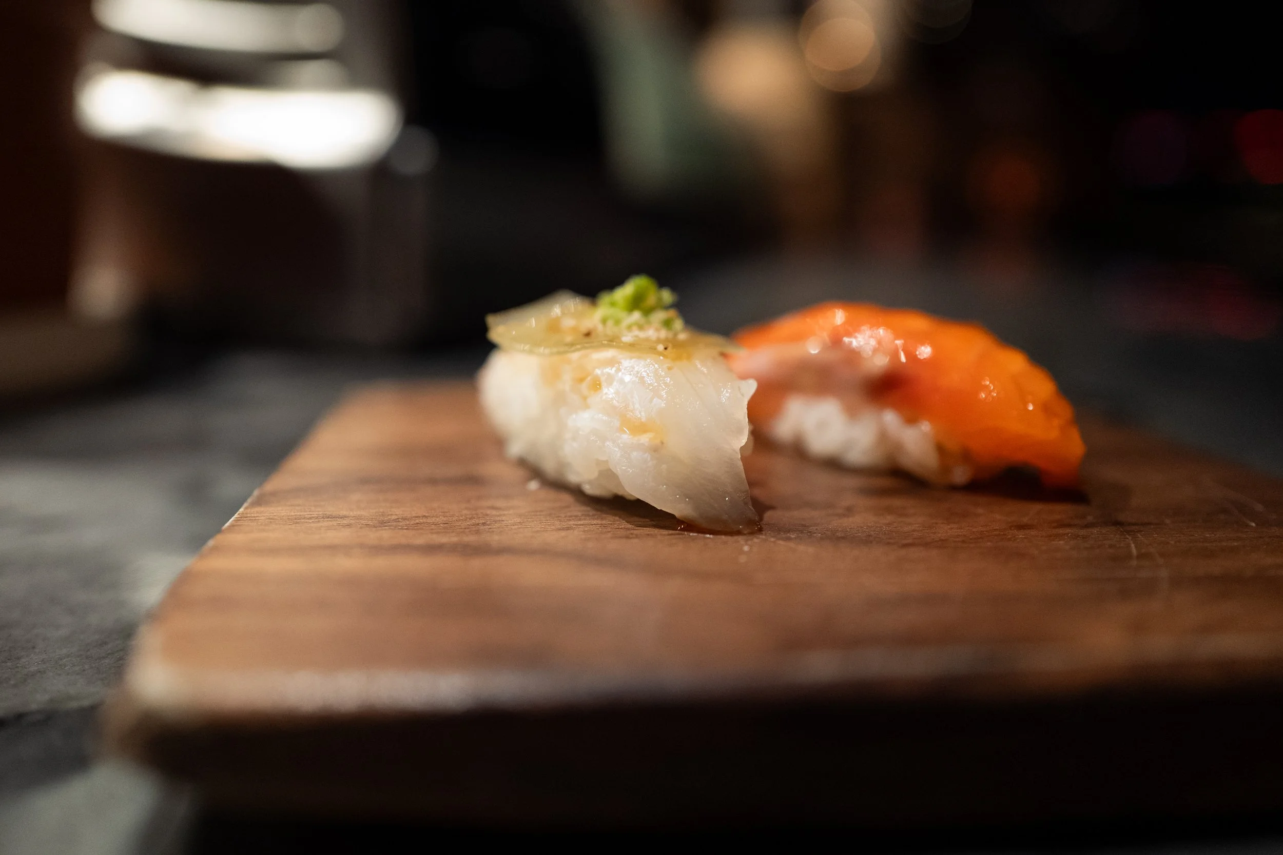 Close-up of two pieces of sushi on a wooden board, with the background blurred.