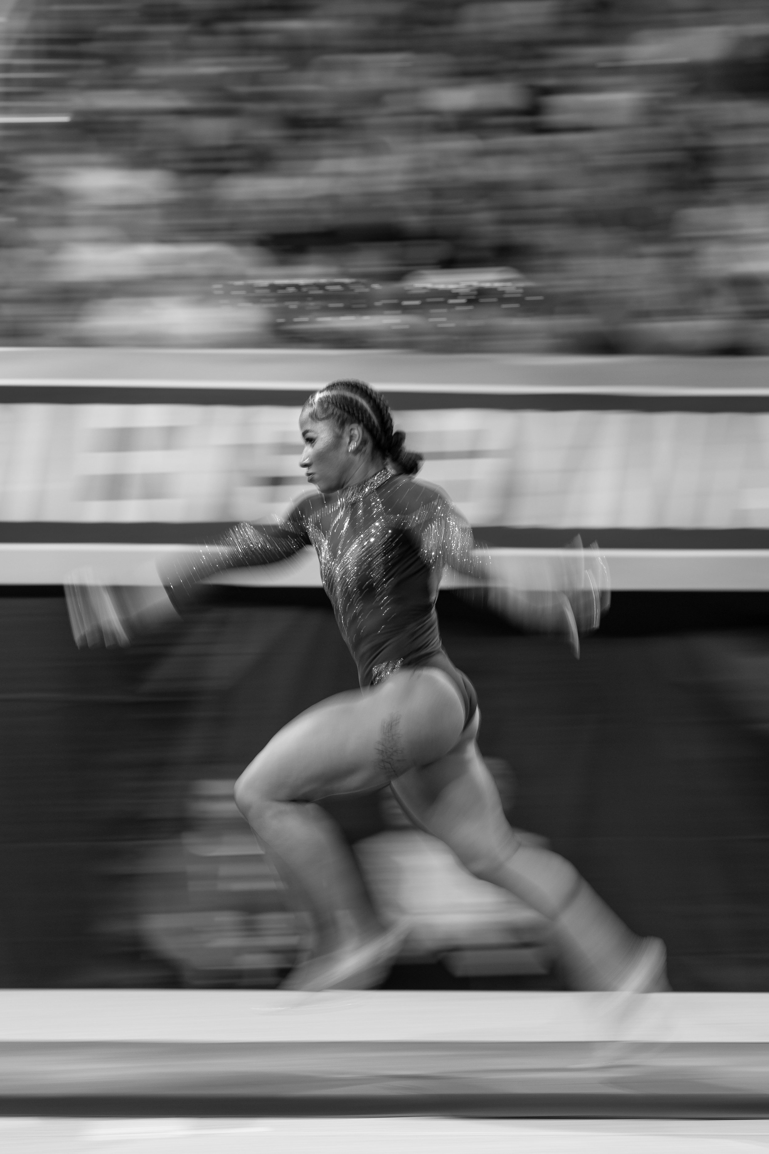 A female figure skater performing a spin in a skating rink, captured in motion blur in black and white.