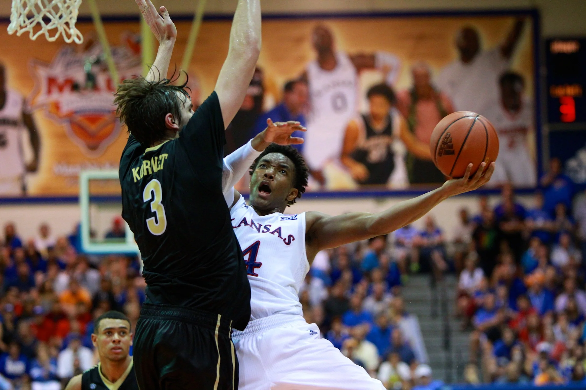 Two basketball players competing for the ball during a game with in a crowded gymnasium.