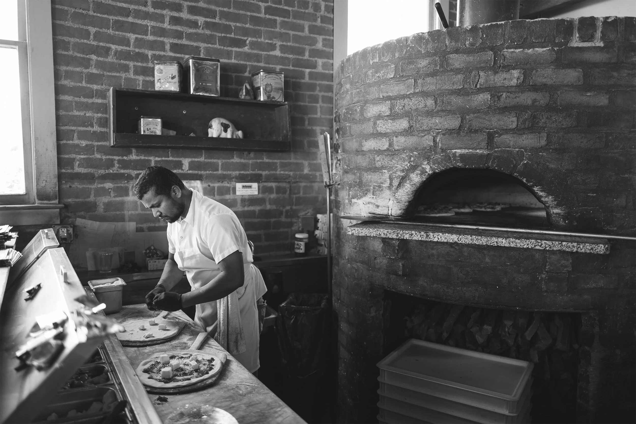 A man making pizza in a rustic kitchen with exposed brick walls and a brick oven.