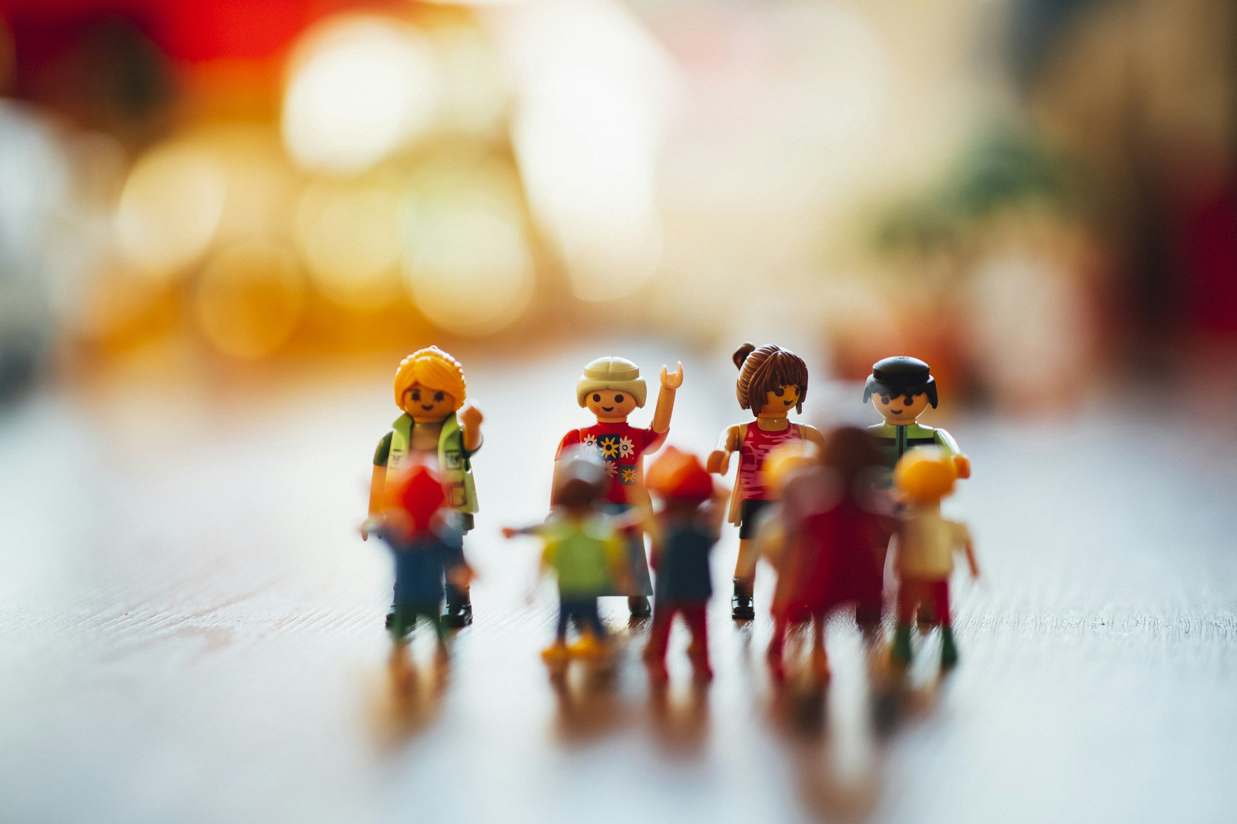 Close-up of colorful toy figurines standing in a row on a reflective surface with blurred, colorful background.