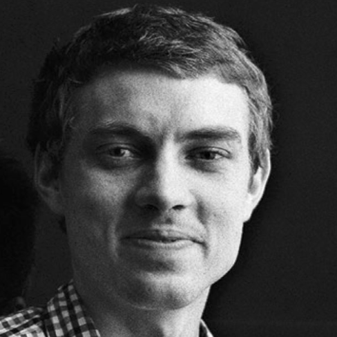 Black and white photo of a young man with short hair, wearing a checkered shirt, looking slightly to the side with a subtle smile.