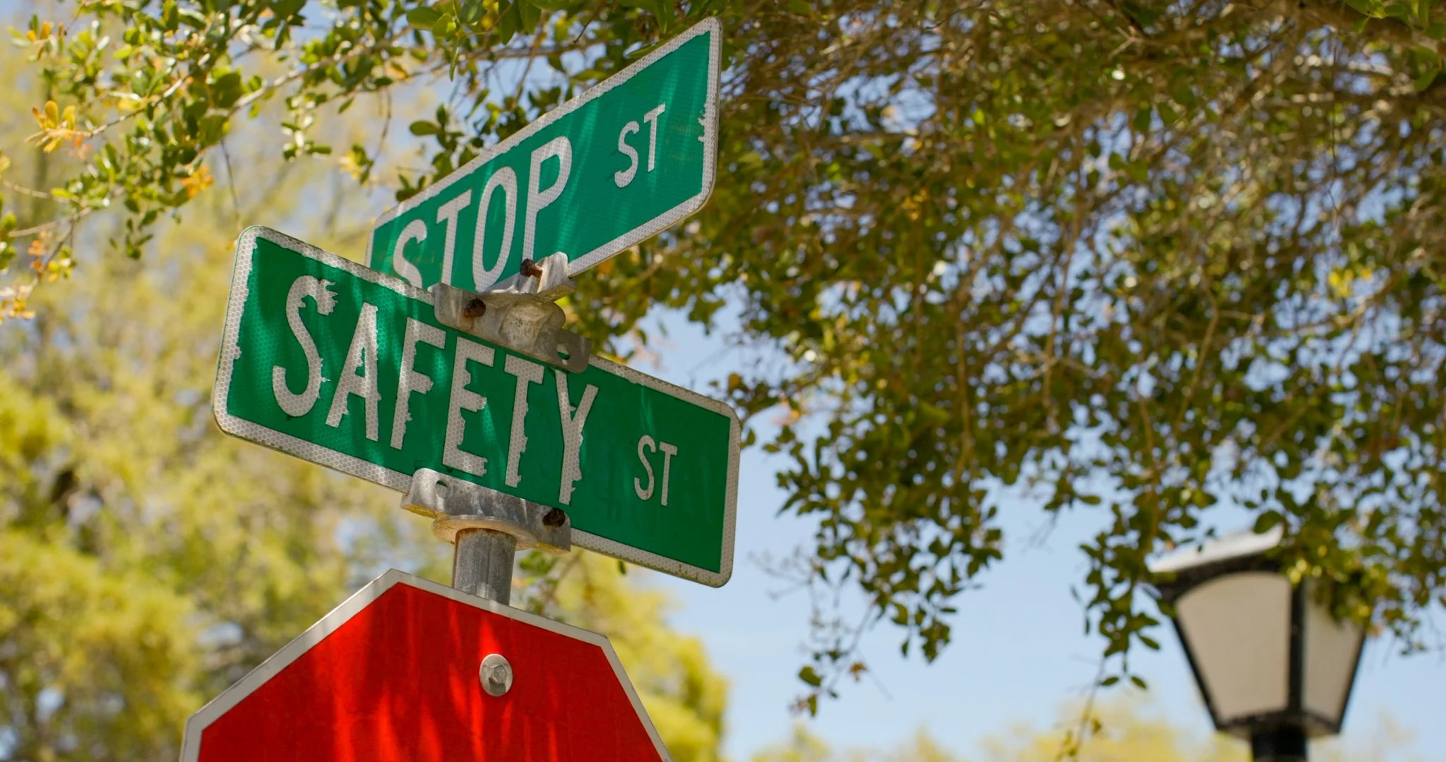 Street signs for Stop Street and Safety Street at an intersection with green foliage in the background.