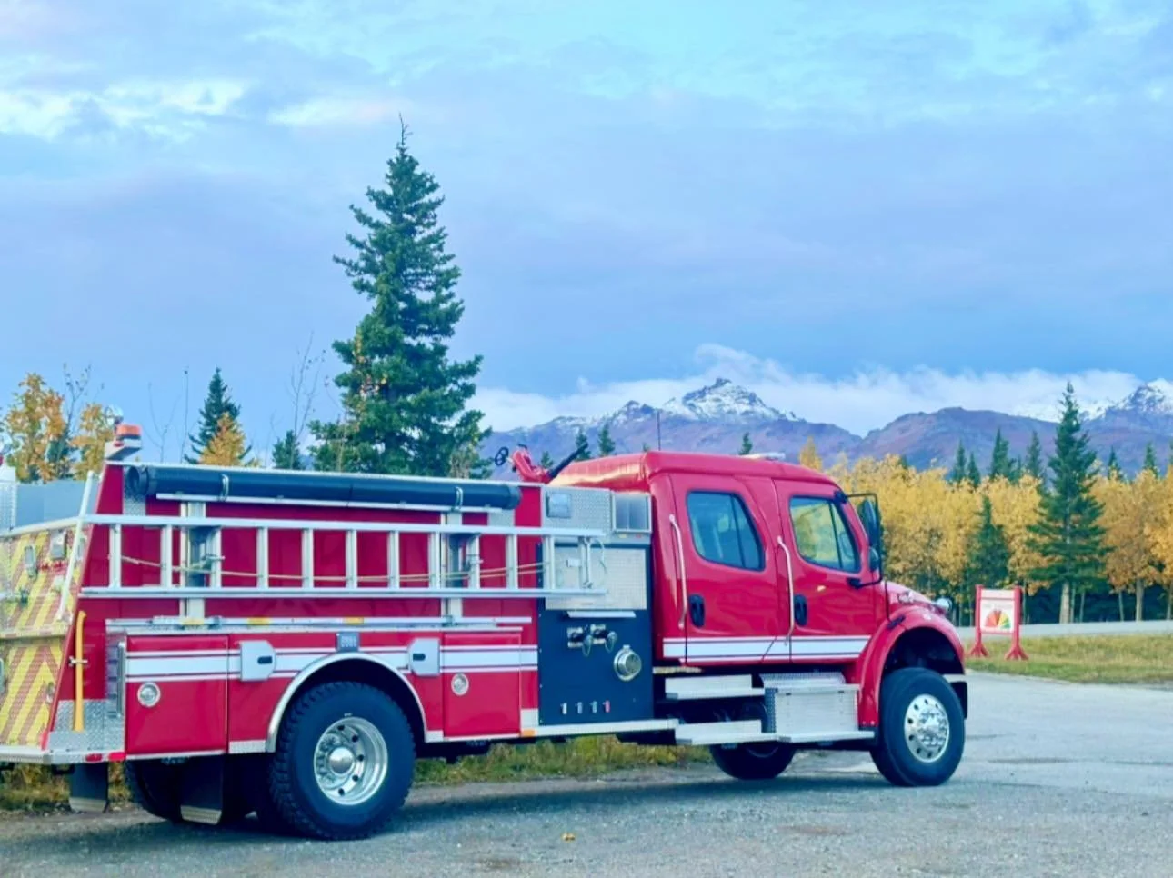 Red fire truck parked on a road with trees and mountain landscape in the background.