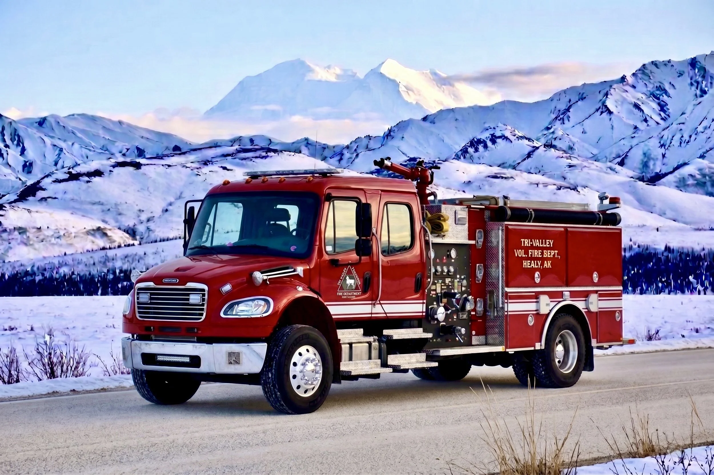 A red fire truck parked on a snowy road with snow-covered mountain peaks in the background.