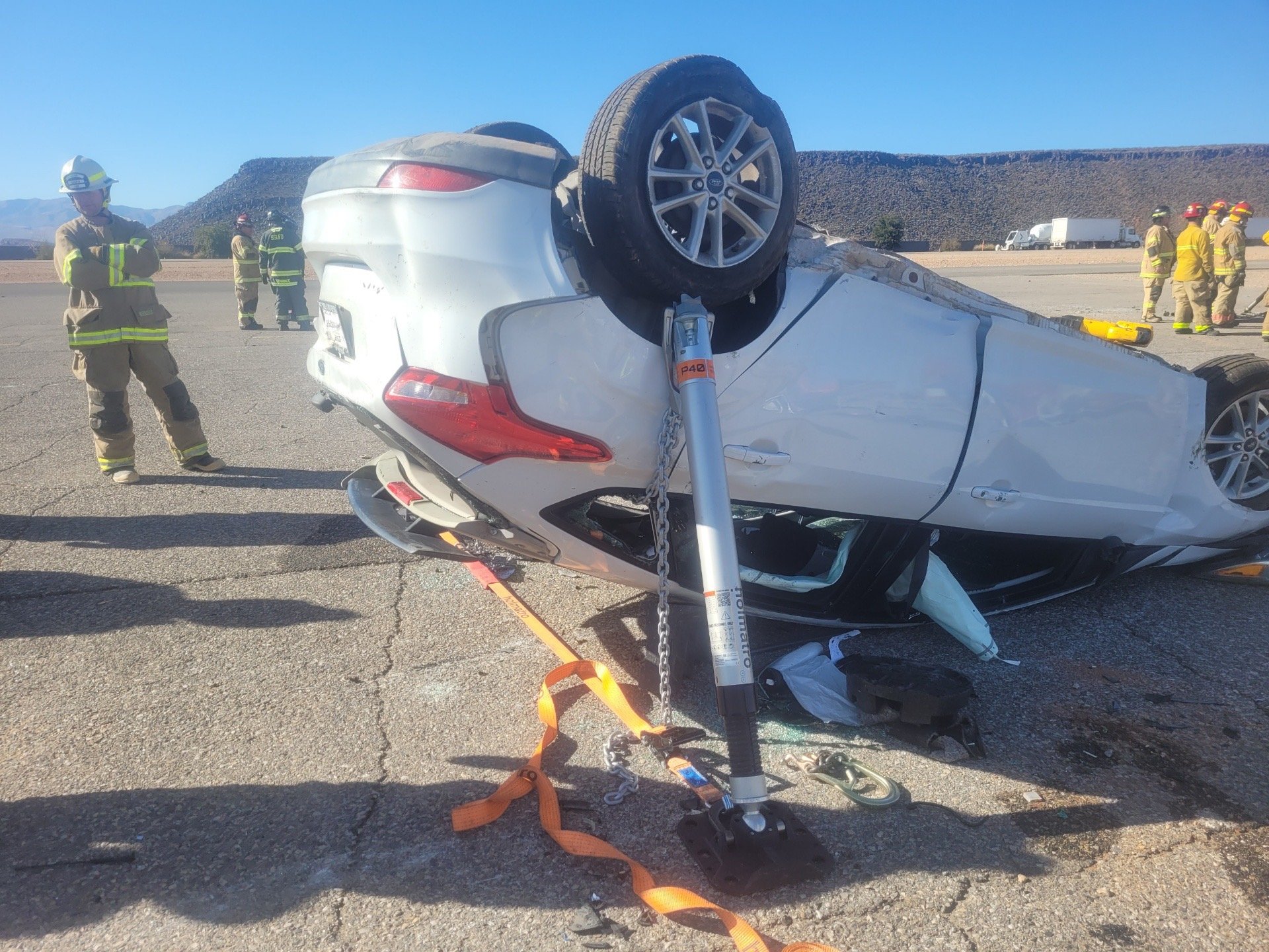 An overturned white car on a highway with firefighters and emergency responders at the scene, used to assist in vehicle extrication and accident response.