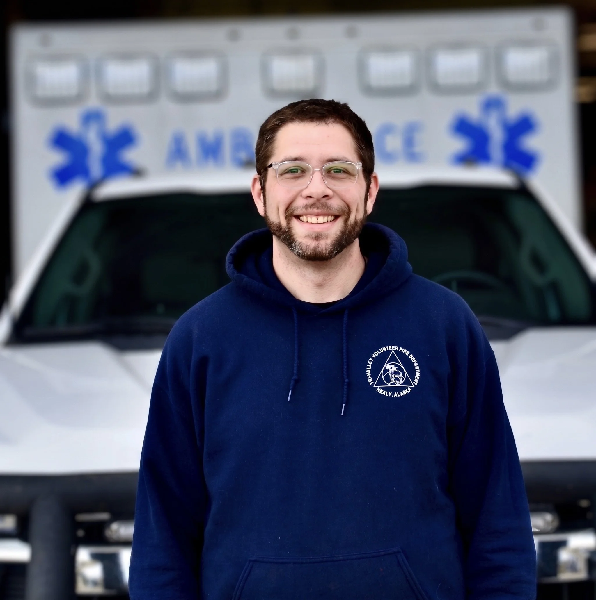Cartoon male paramedic with a beard, wearing a white uniform and helmet with a red cross, holding a medical kit.