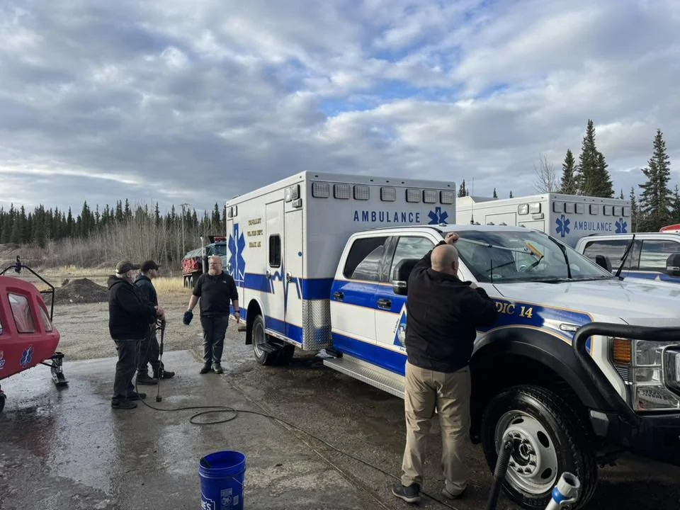 Emergency medical personnel and crew members preparing an ambulance vehicle outdoors on a cloudy day.