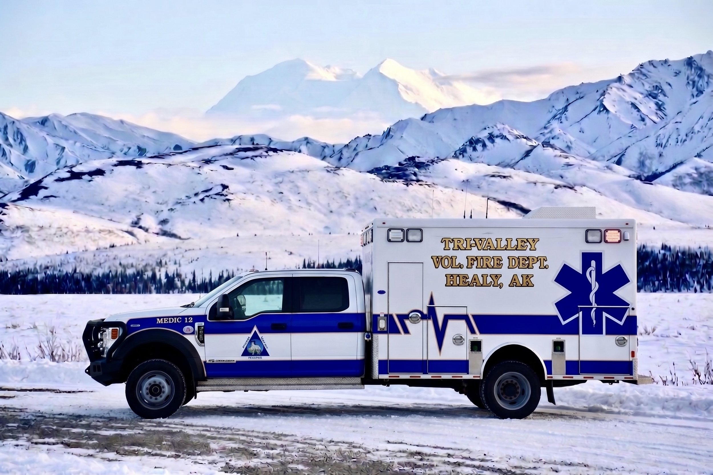 A white ambulance with blue and gold markings parked on snowy terrain with snow-covered mountains in the background.