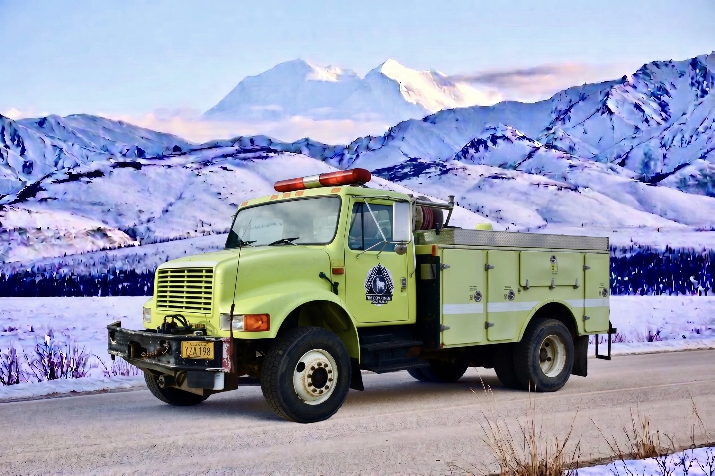 A yellow fire truck with a ladder and siren parked on a snow-covered road in front of snow-capped mountains and a clear sky.