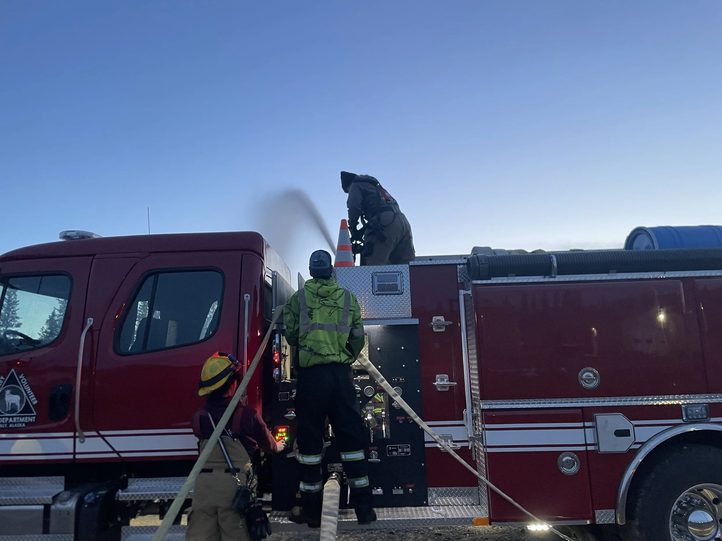 Firefighters and emergency responders working with a fire truck, preparing equipment during daylight hours.