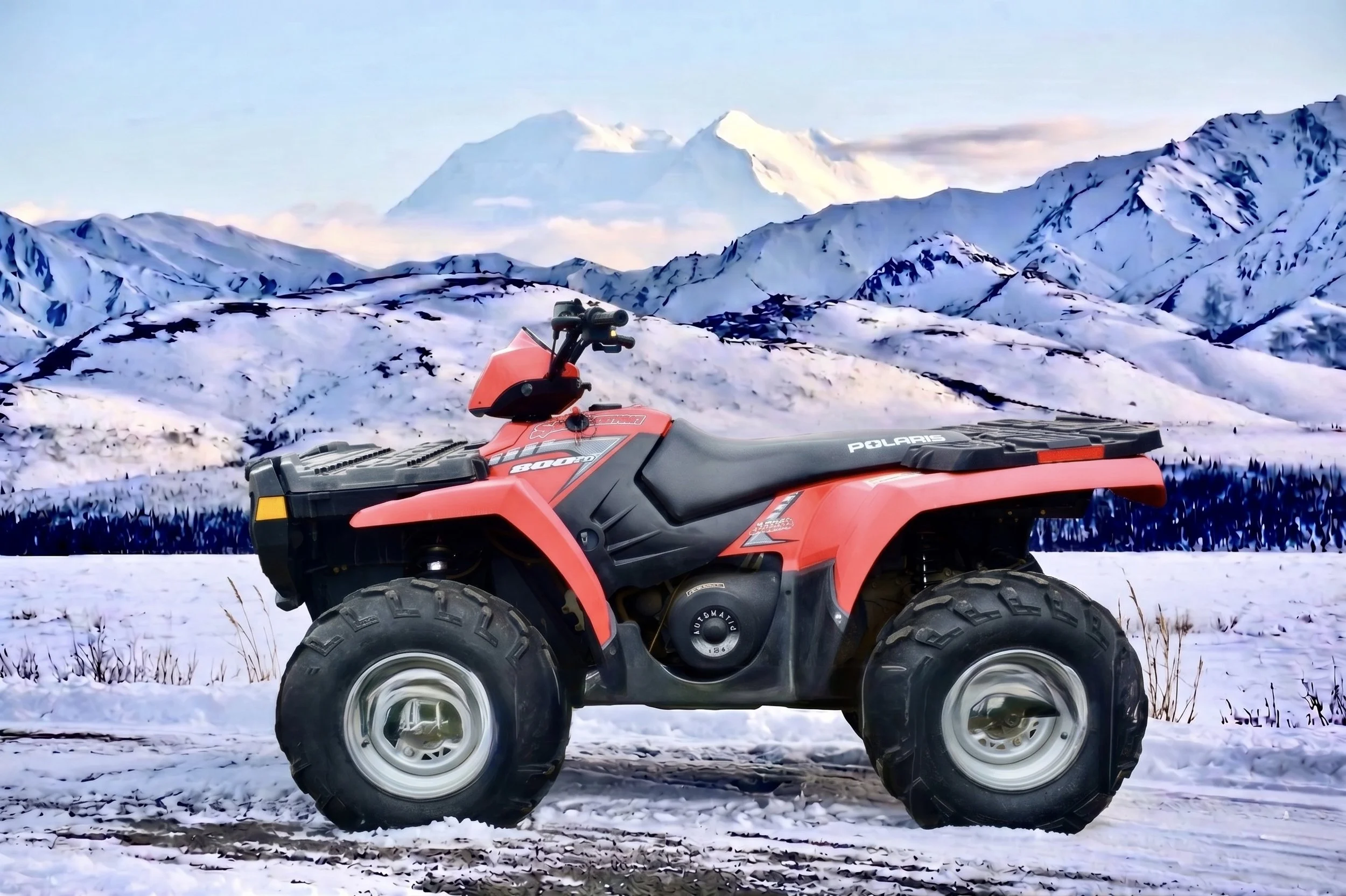 A red all-terrain vehicle parked on snow with snow-covered mountains and a partly cloudy sky in the background.
