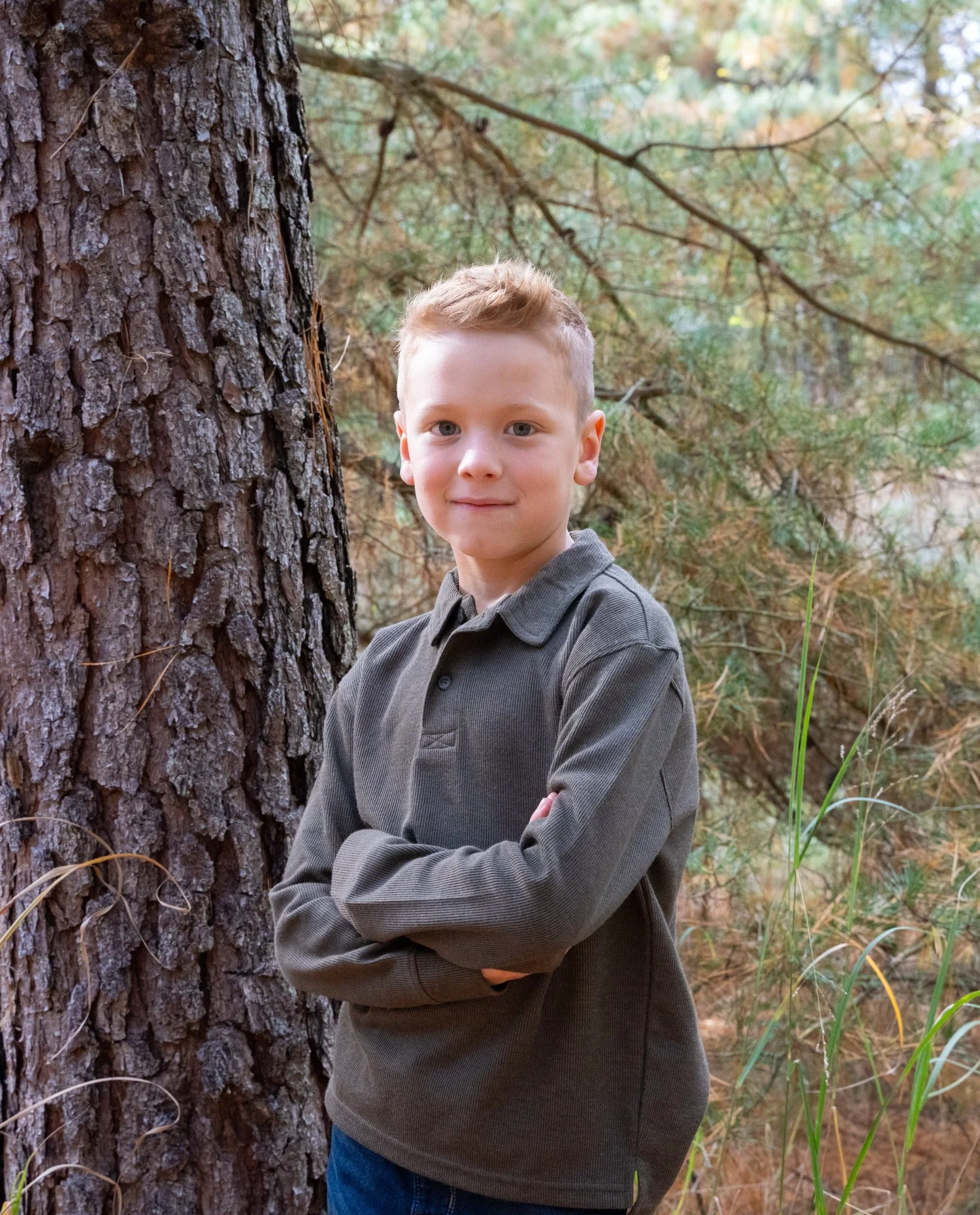 Older boy leaning against a pine tree with arms crossed