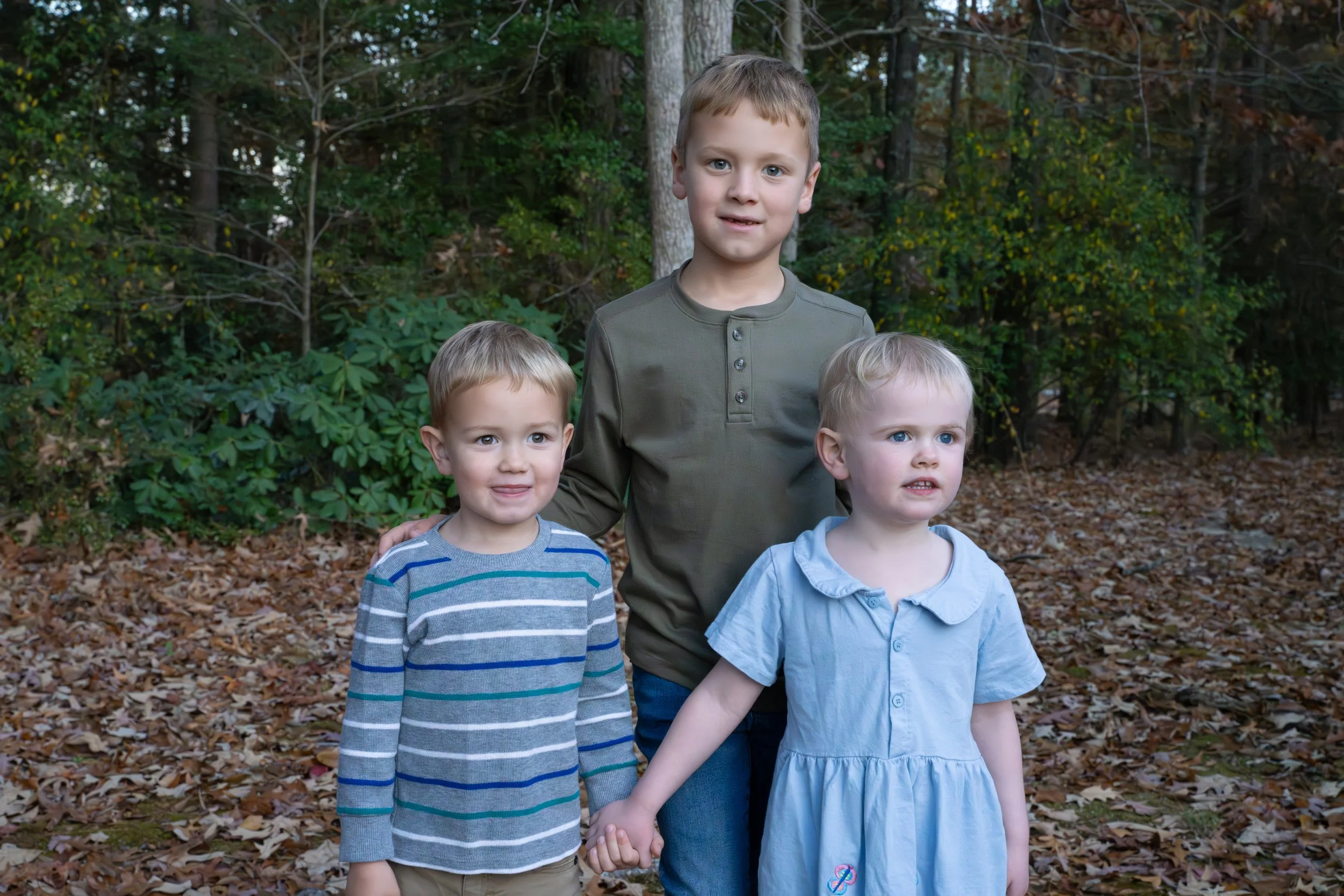 Three children posing together in matching neutral outfits outdoors