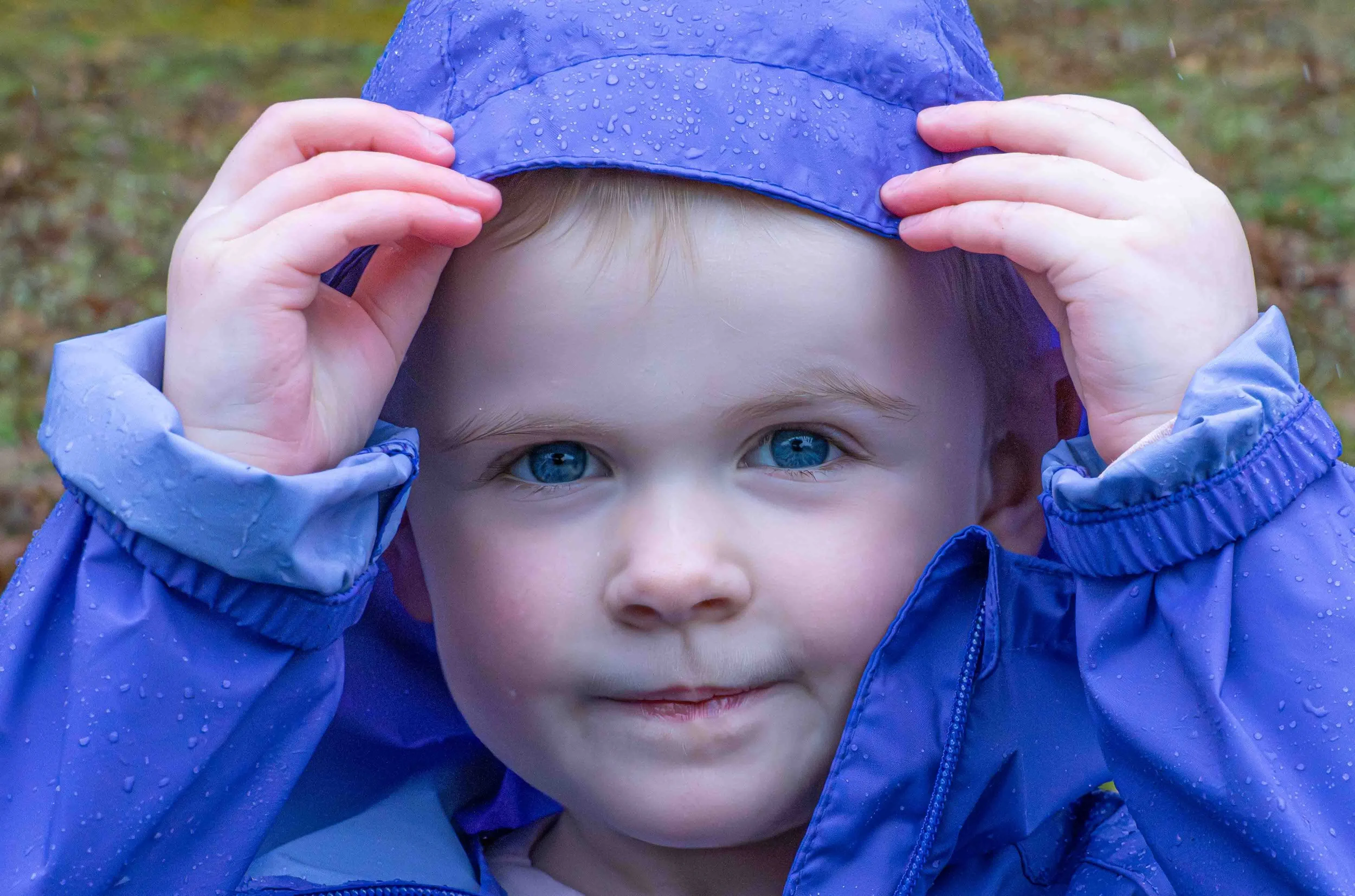 Child in blue hooded jacket peeking out with hands near face