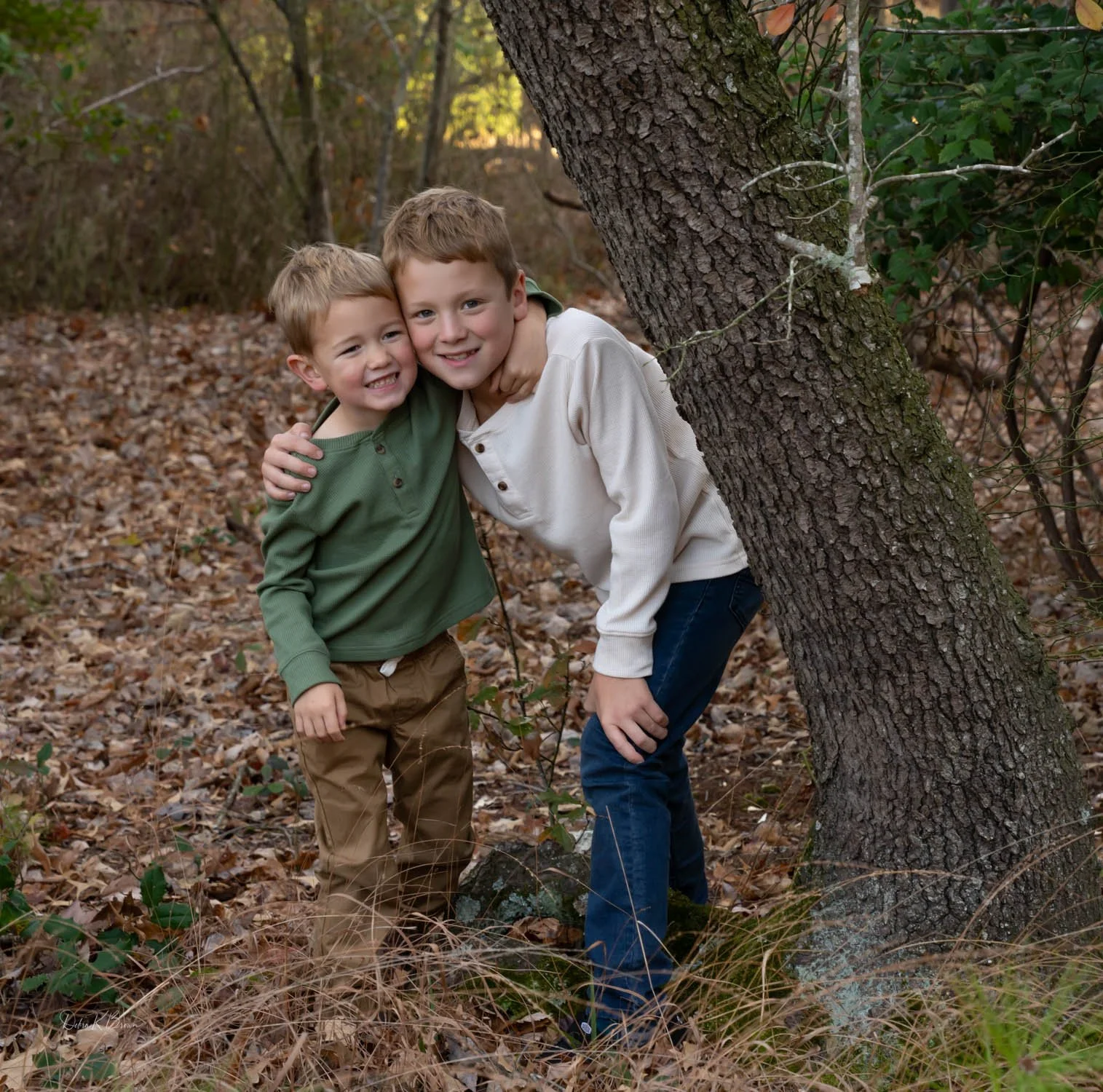 Two children hugging playfully among trees in the woods