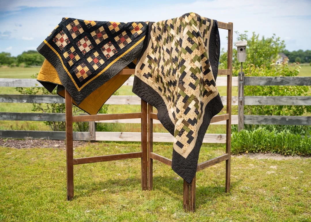 Blanket draped over a wooden clothes drying rack outdoors in a grassy area with a wooden fence and trees in the background.