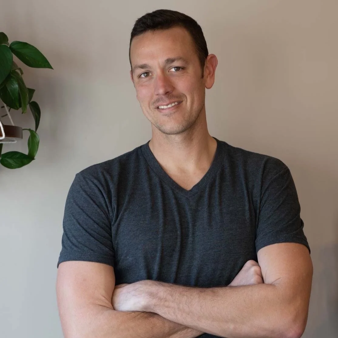 Man in gray t-shirt smiling with arms crossed indoors