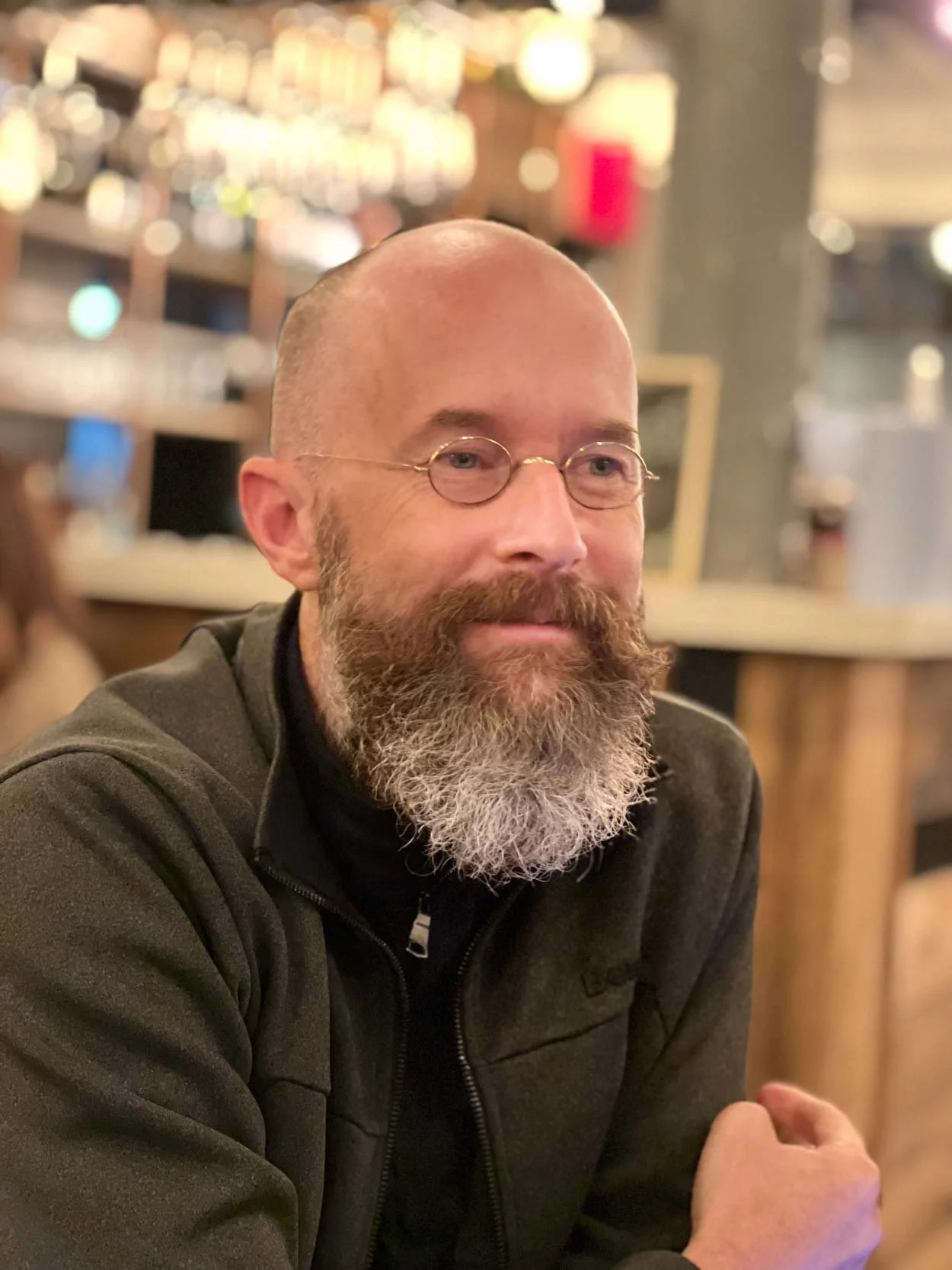 Man with beard sitting indoors, smiling slightly