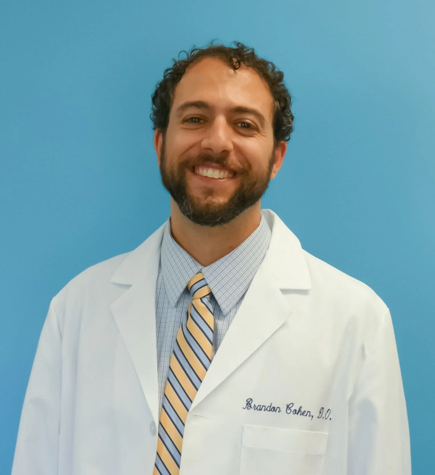Man in lab coat smiling in front of a blue background