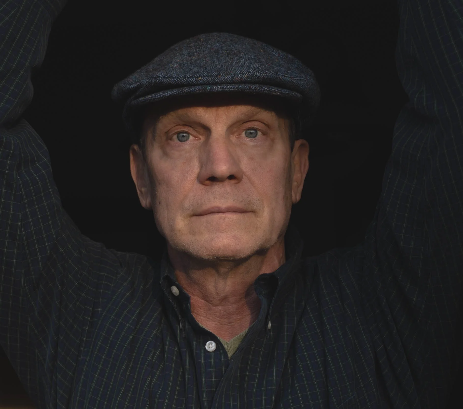 Older man in a black shirt and cap looking serious