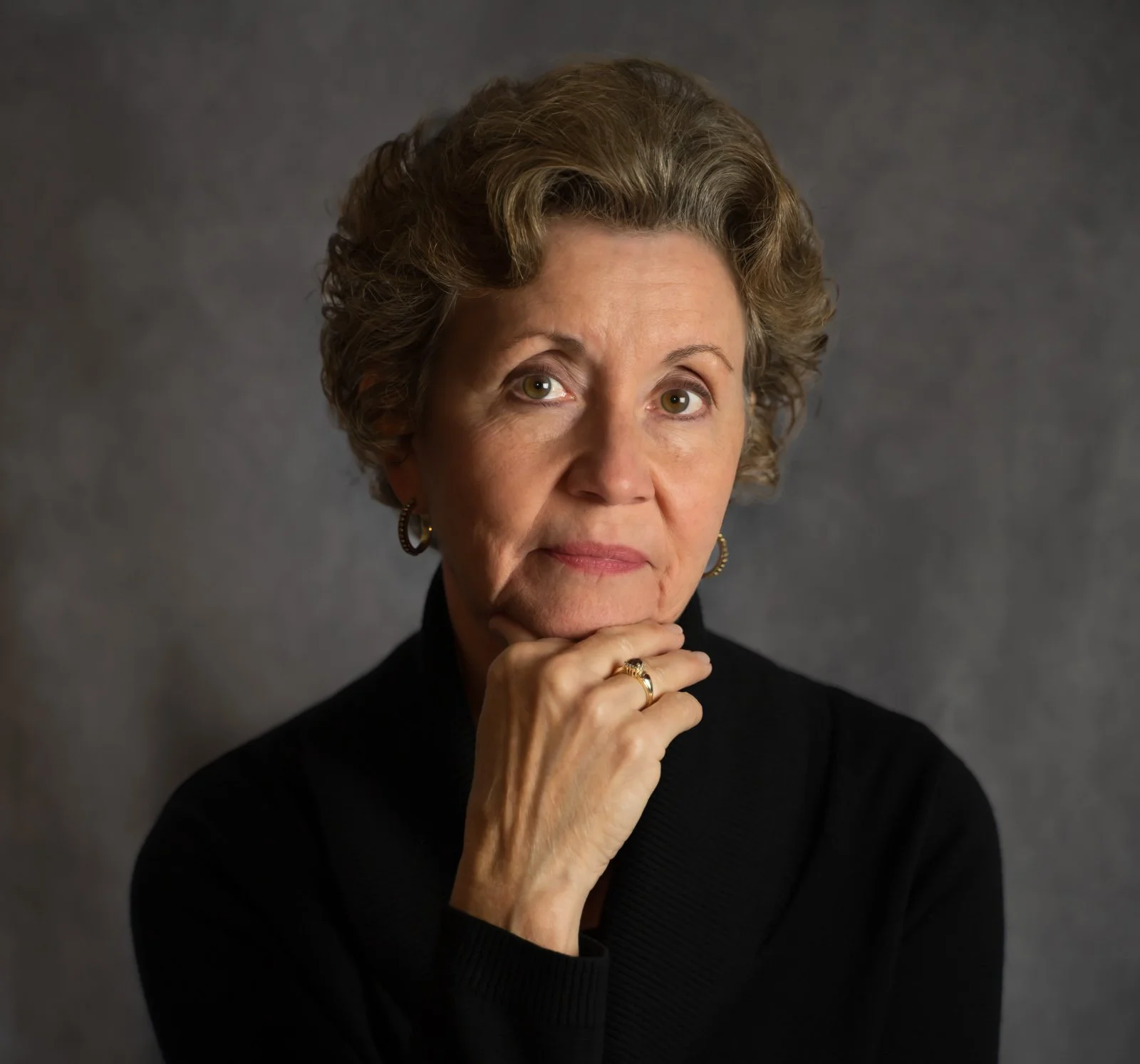 Woman with curly hair resting chin on hand, studio portrait