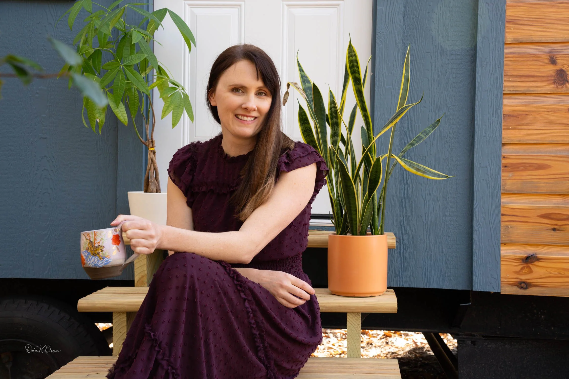 Woman seated indoors beside houseplants, smiling
