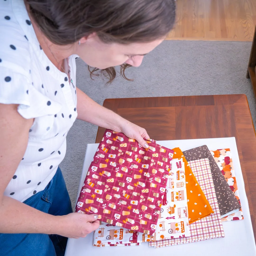 A woman looking at a selection of fabric swatches on a table, with various patterns and colors including red, orange, black, and white.