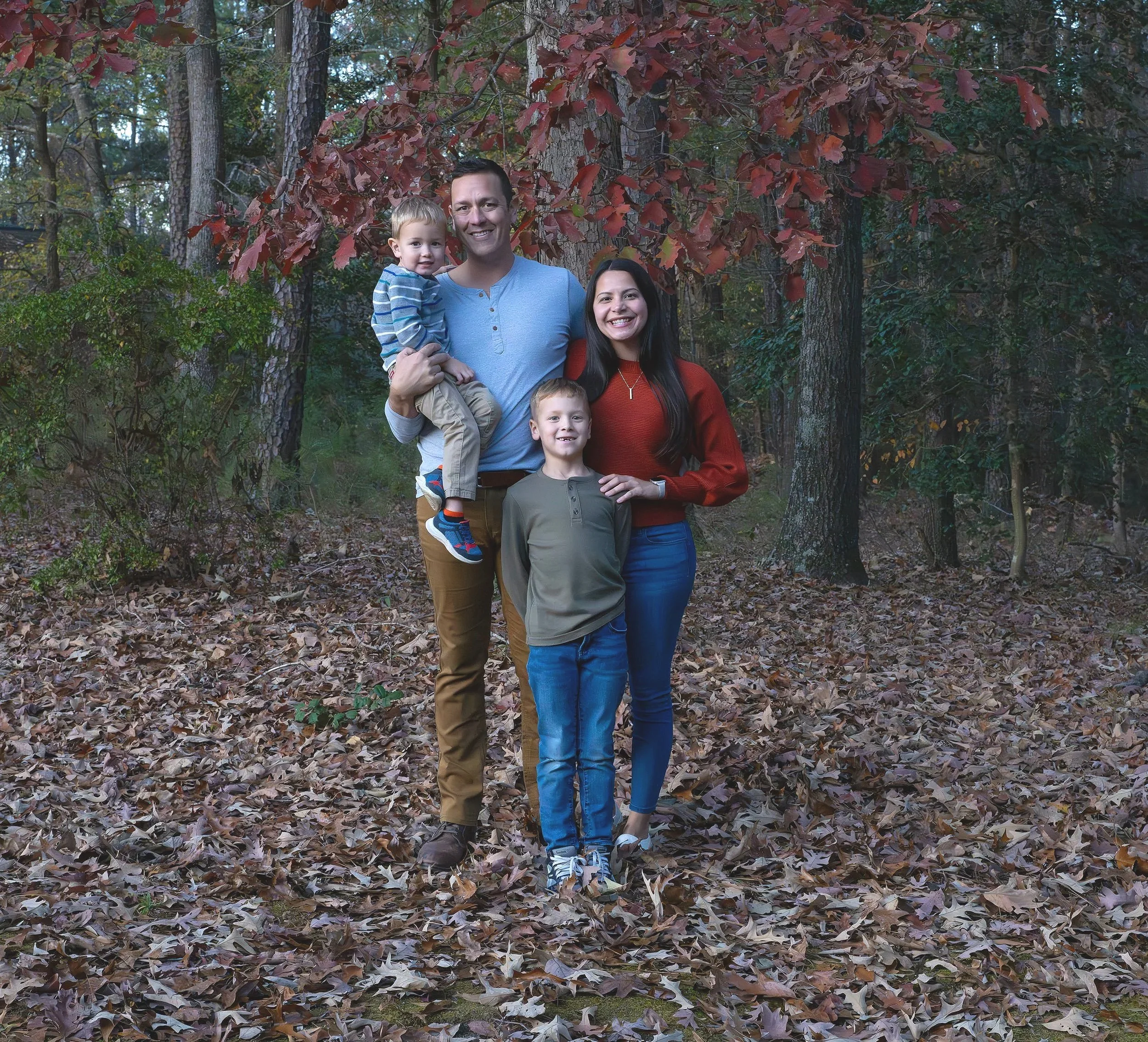 Fall family photo session showing family standing among trees and fallen leaves.