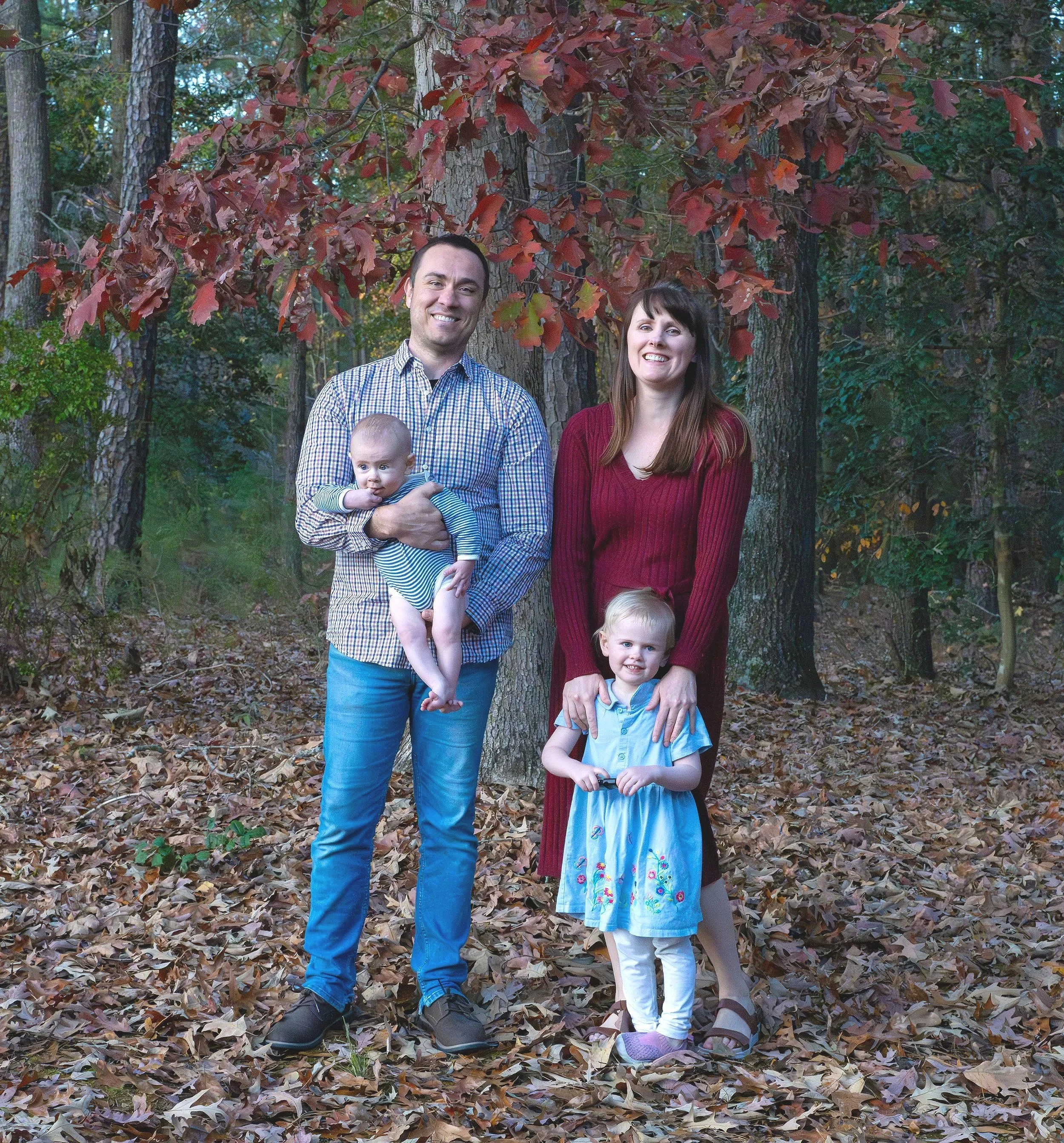 Fall family photo session showing family of four standing in a wooded area with autumn leaves
